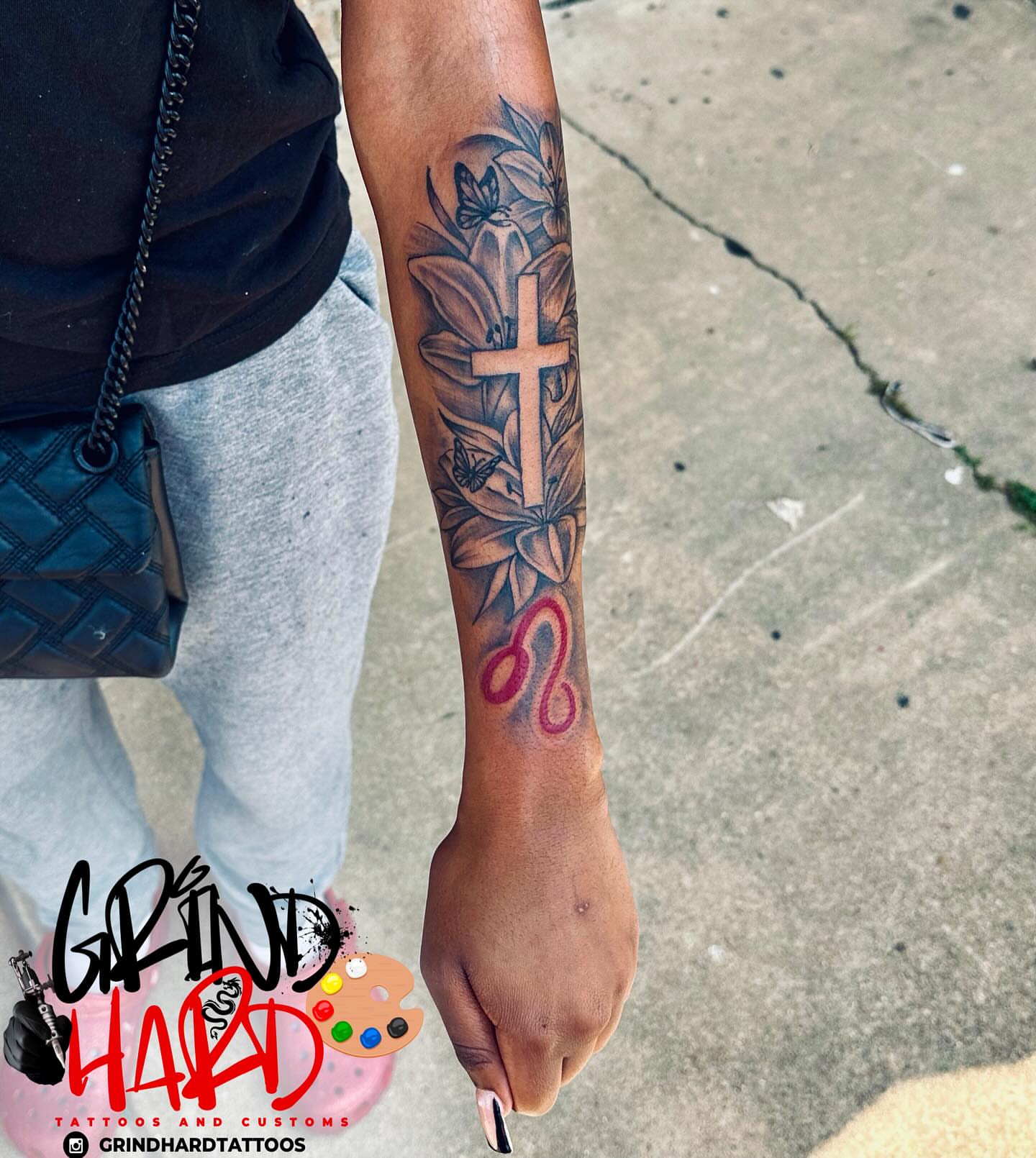 Cross and floral black and grey tattoo on the forearm by GrindHard Quen