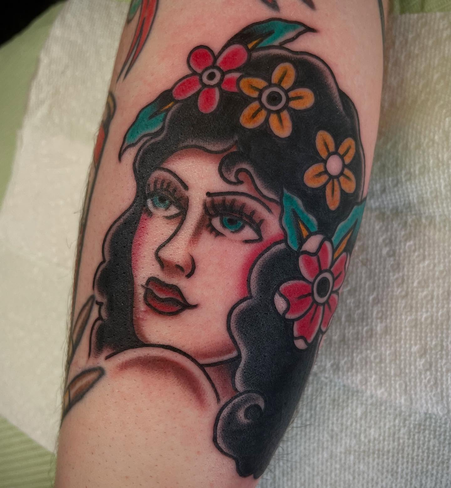 Woman with flowers American traditional tattoo on the forearm by Micheal McGlinchey