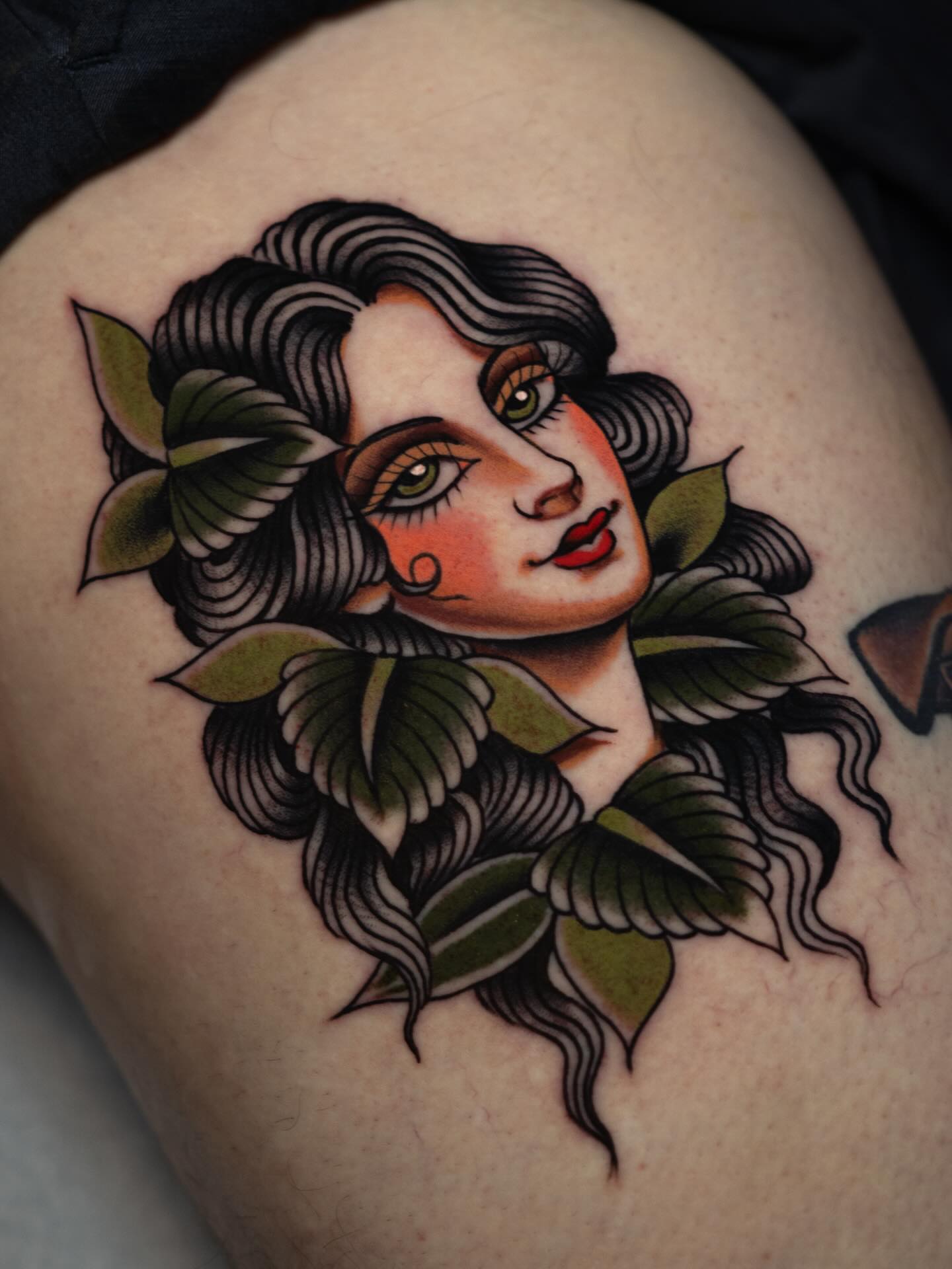 Woman with leaves American traditional tattoo on the thigh by Danny Derrick, San Luis Obispo, California