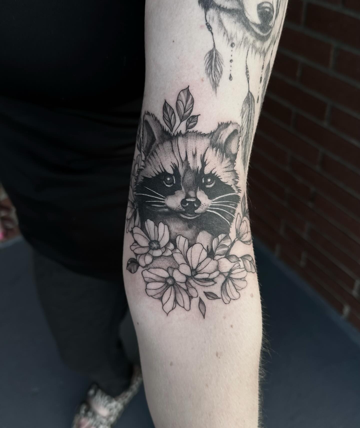 Raccoon and flowers realism tattoo on the forearm by Emmy