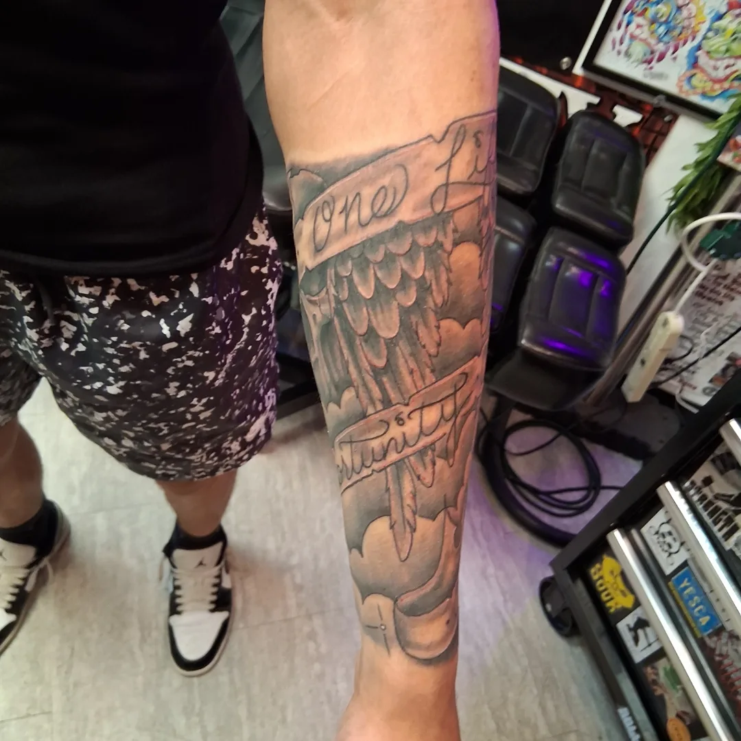 Wings and text American traditional tattoo on the forearm by Dave Johnson, Billings, Montana