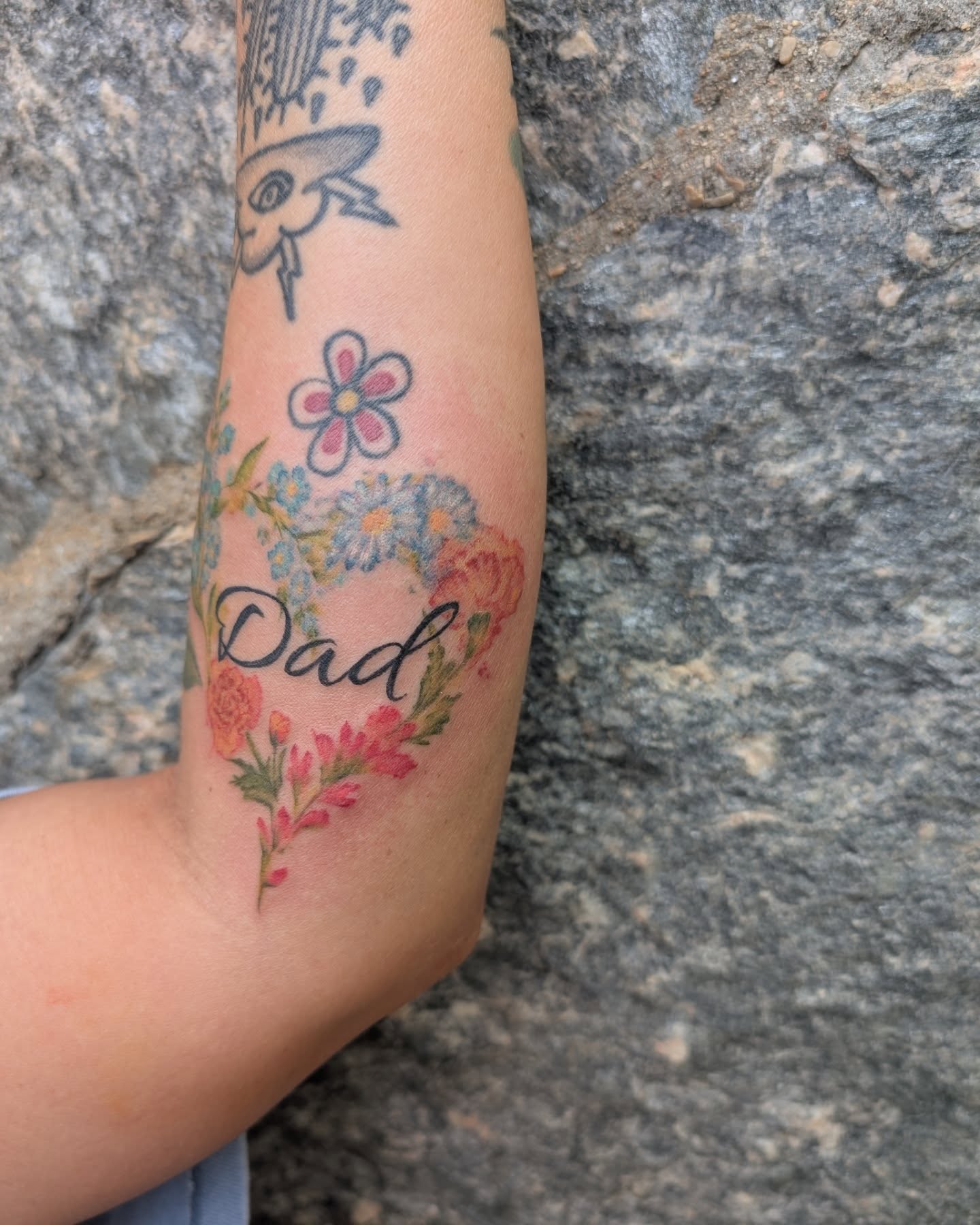 Flowers and 'Dad' new school tattoo on the forearm by Cat