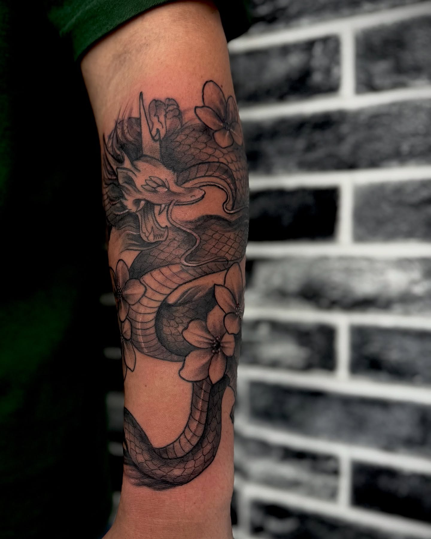 Dragon and flowers realism tattoo on the forearm by Mitsuko Ching