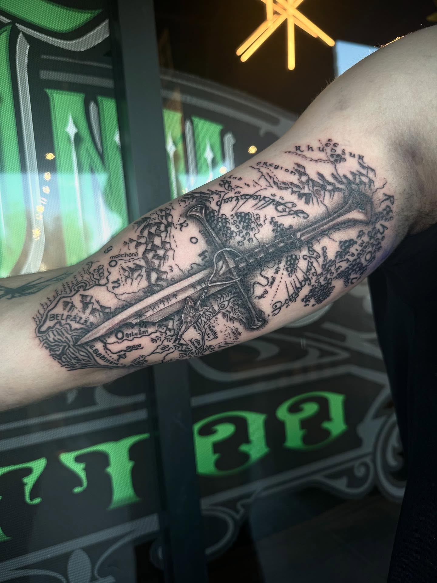 Map and sword black and grey tattoo on the forearm by Jianna