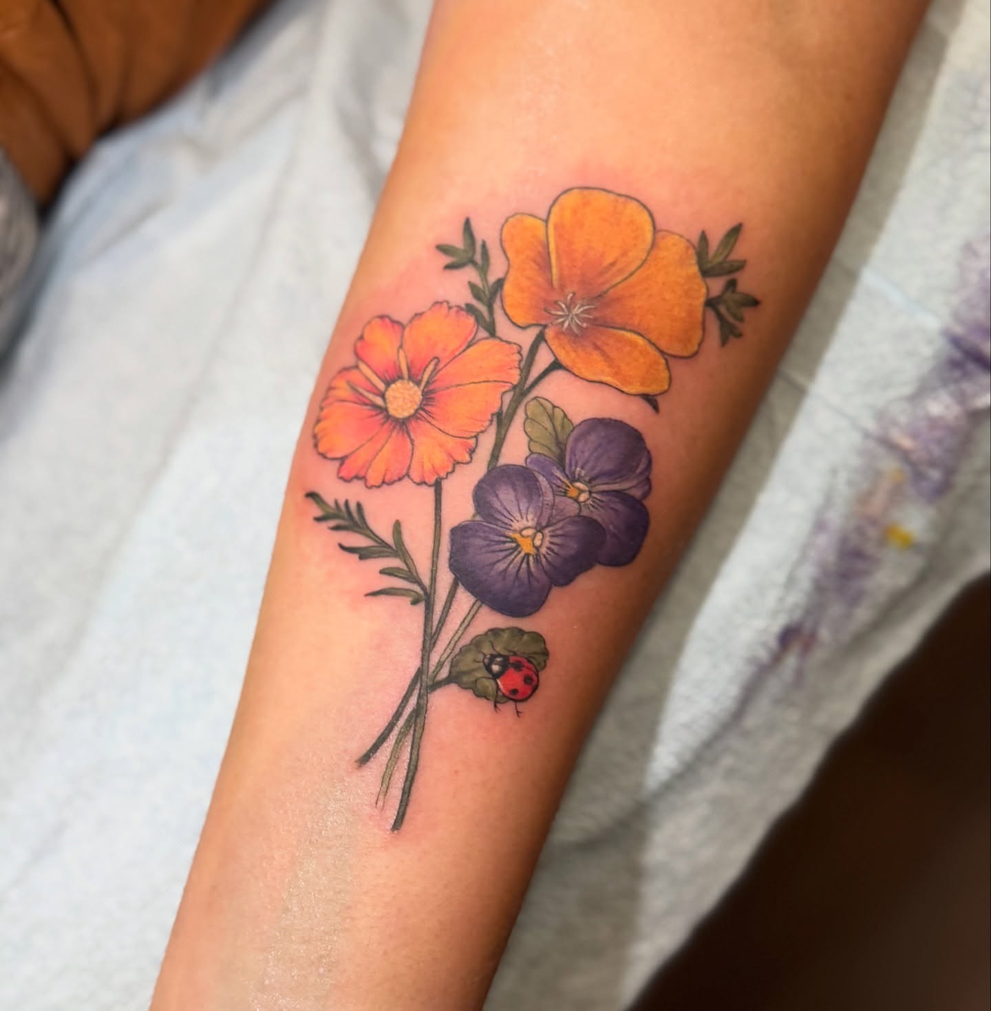 Flowers and ladybug realism tattoo on the forearm by đź’›Kristinađź’› tattoos with intention, Minneapolis, Minnesota