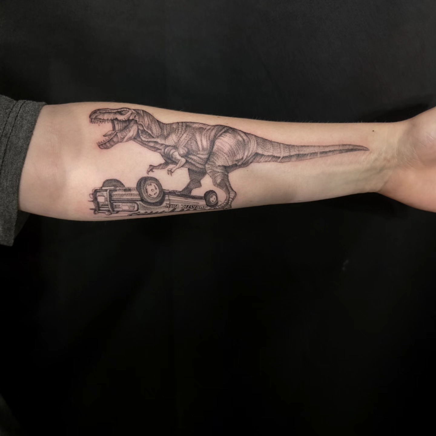 T-Rex riding car black and grey tattoo on the forearm by Utah Tattoo Artist