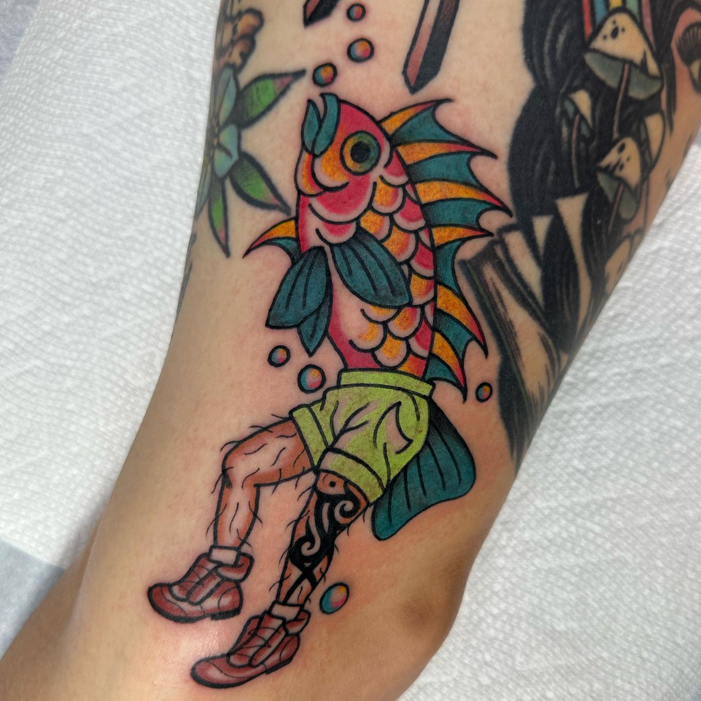 Fish wearing shorts American traditional tattoo on the forearm by Alexa Wolfkiel