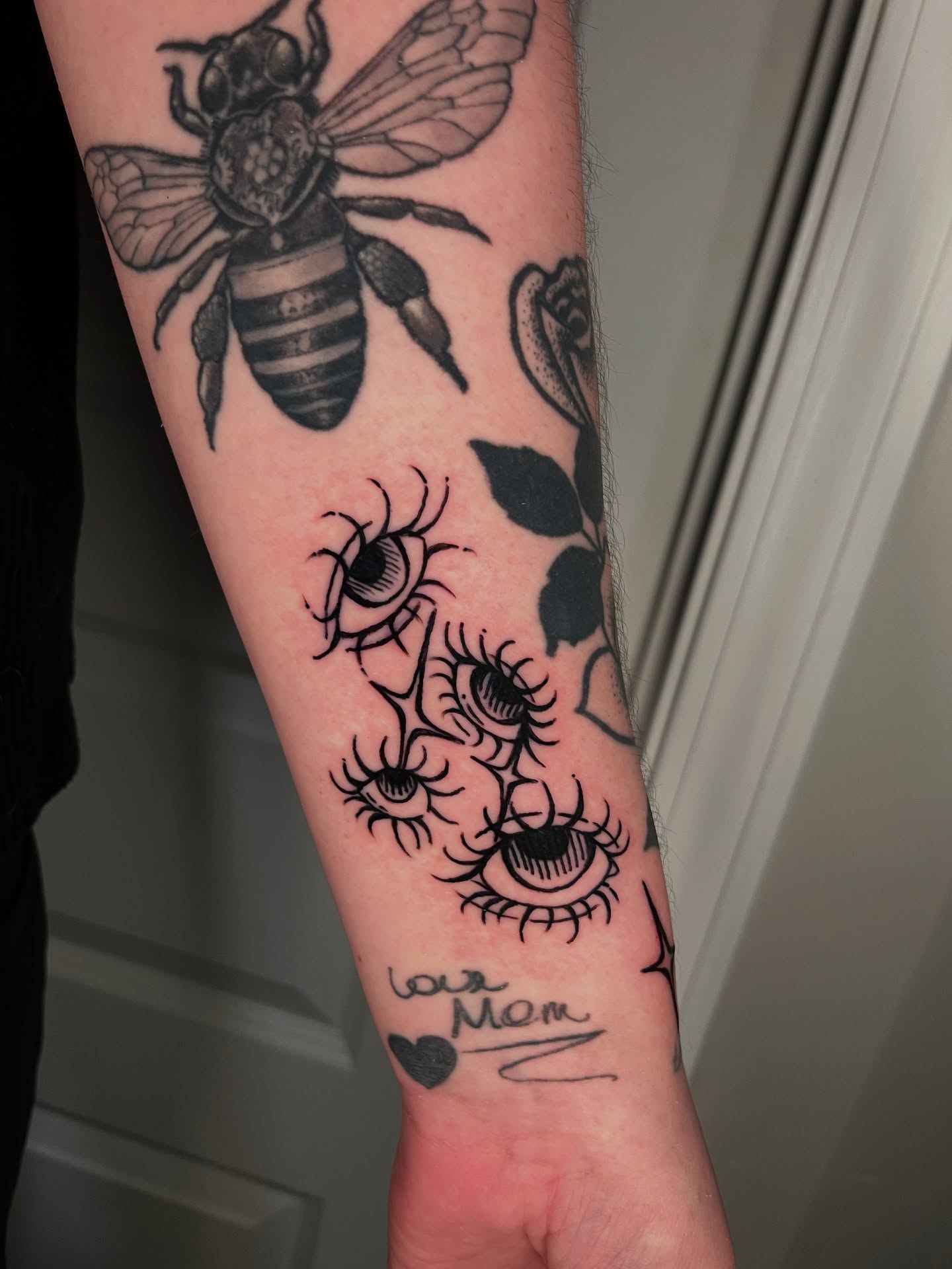 Eyes and bee black and grey tattoo on the forearm by layne