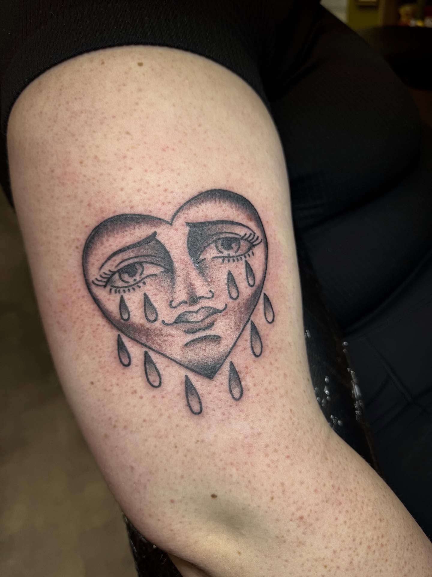 Heart with crying face black and grey tattoo on the thigh by 𝗞𝗮𝘁 𝗕𝗹𝗮𝗻𝗸𝗲𝗻𝘀𝗵𝗶𝗽