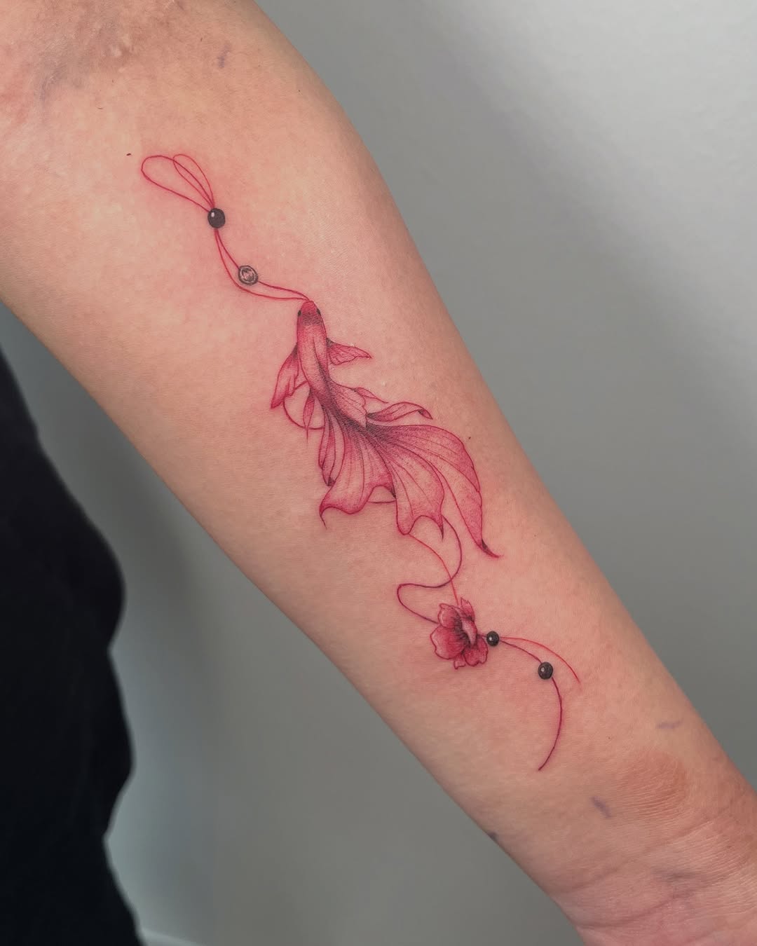 Fish with red string and flower fine line tattoo on the forearm by kt