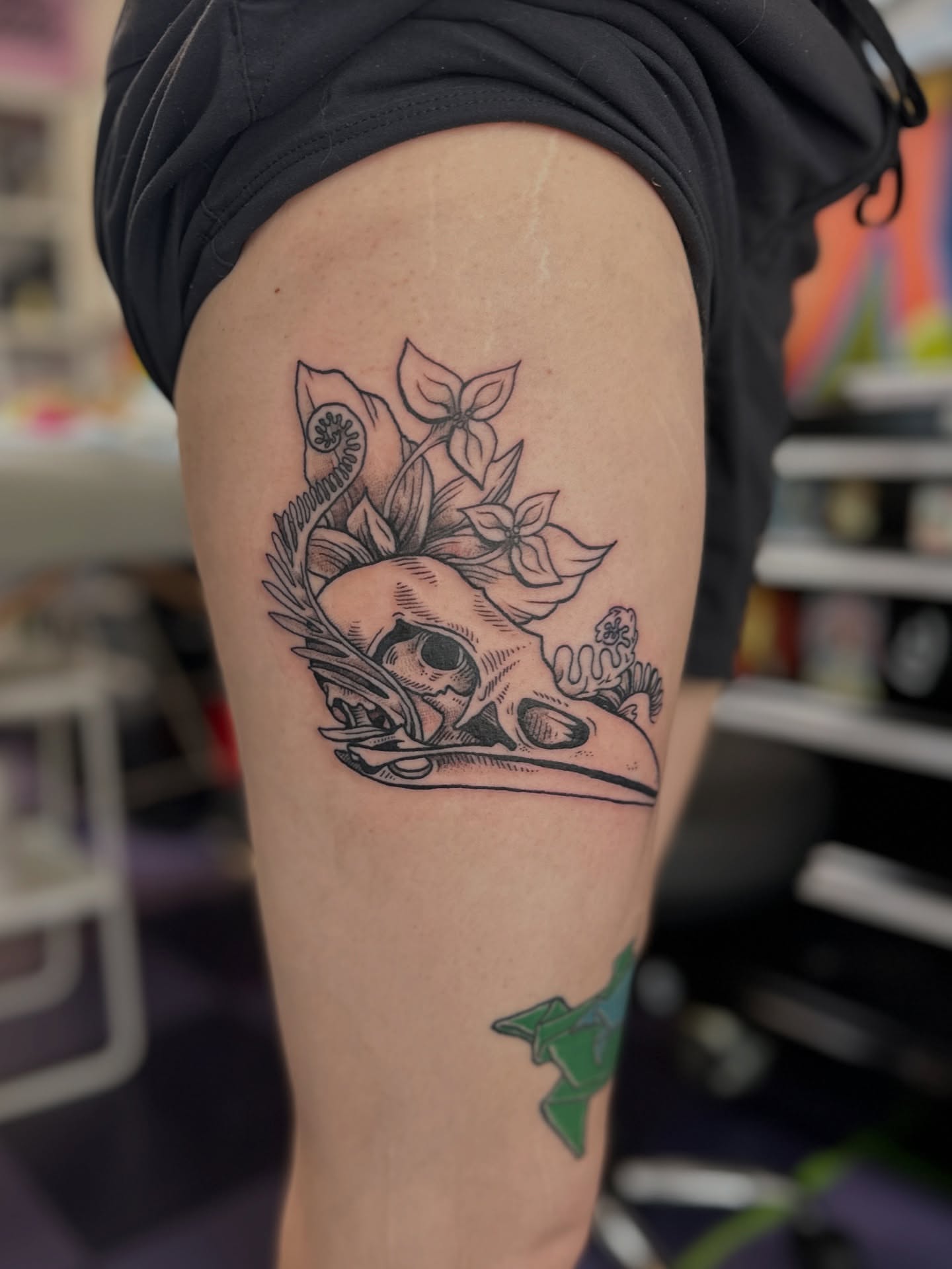 Skull with flowers black and grey tattoo on the thigh by Emma Berger