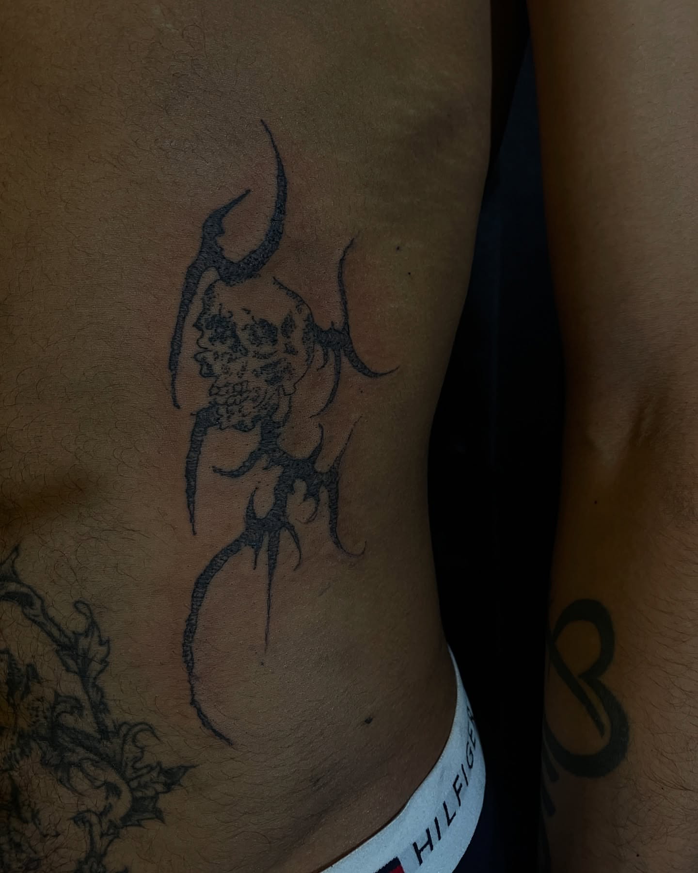 Skull with horns black and grey tattoo on the ribs by ɴᴏᴍᴢ ᴅʏsᴇᴍʙᴏᴅɪᴍᴇɴᴛ