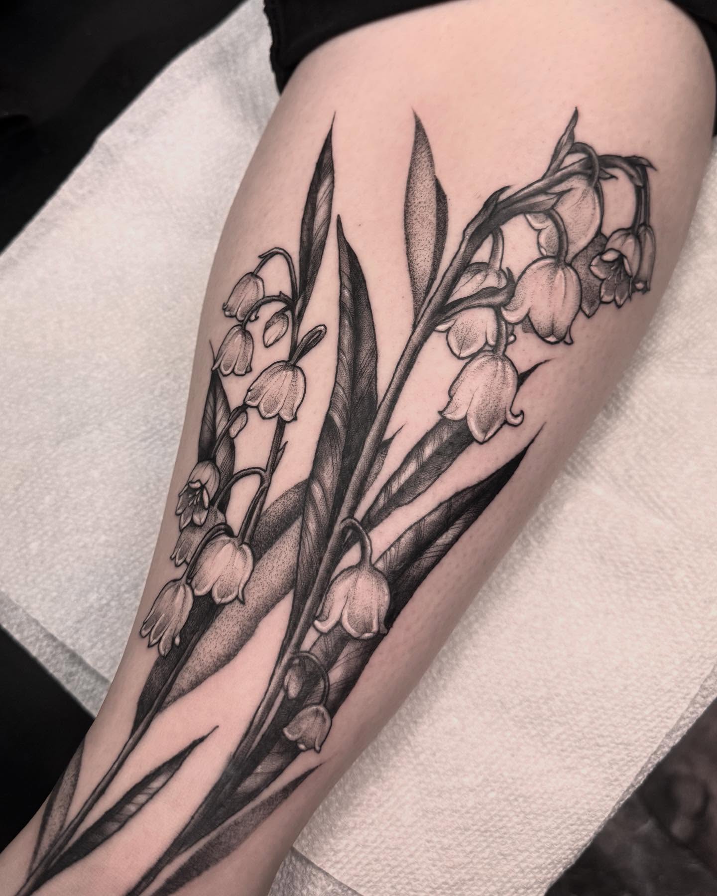 Lily of the valley black and grey tattoo on the thigh by 𝔈𝔯𝔦𝔫 𝔊𝔦𝔩𝔩𝔦𝔩𝔞𝔫𝔡, Springfield, Ohio