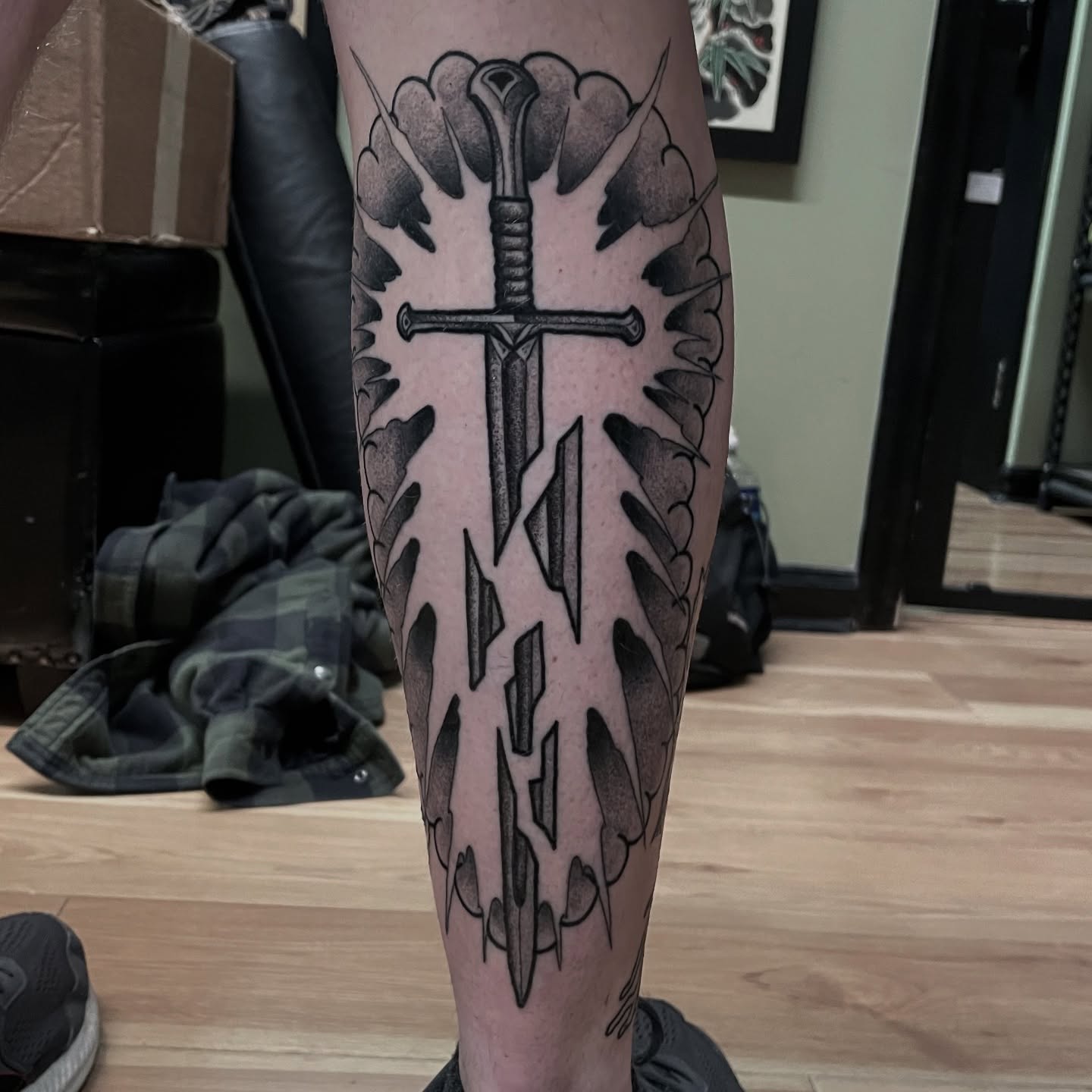 Sword and wings black and grey tattoo on the calf by Ian Spong