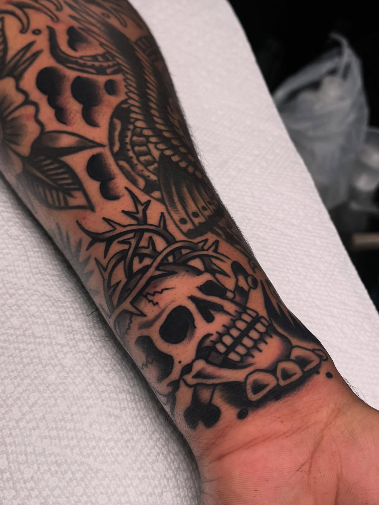 Skull and floral black and grey tattoo on the forearm by Ryan Engels