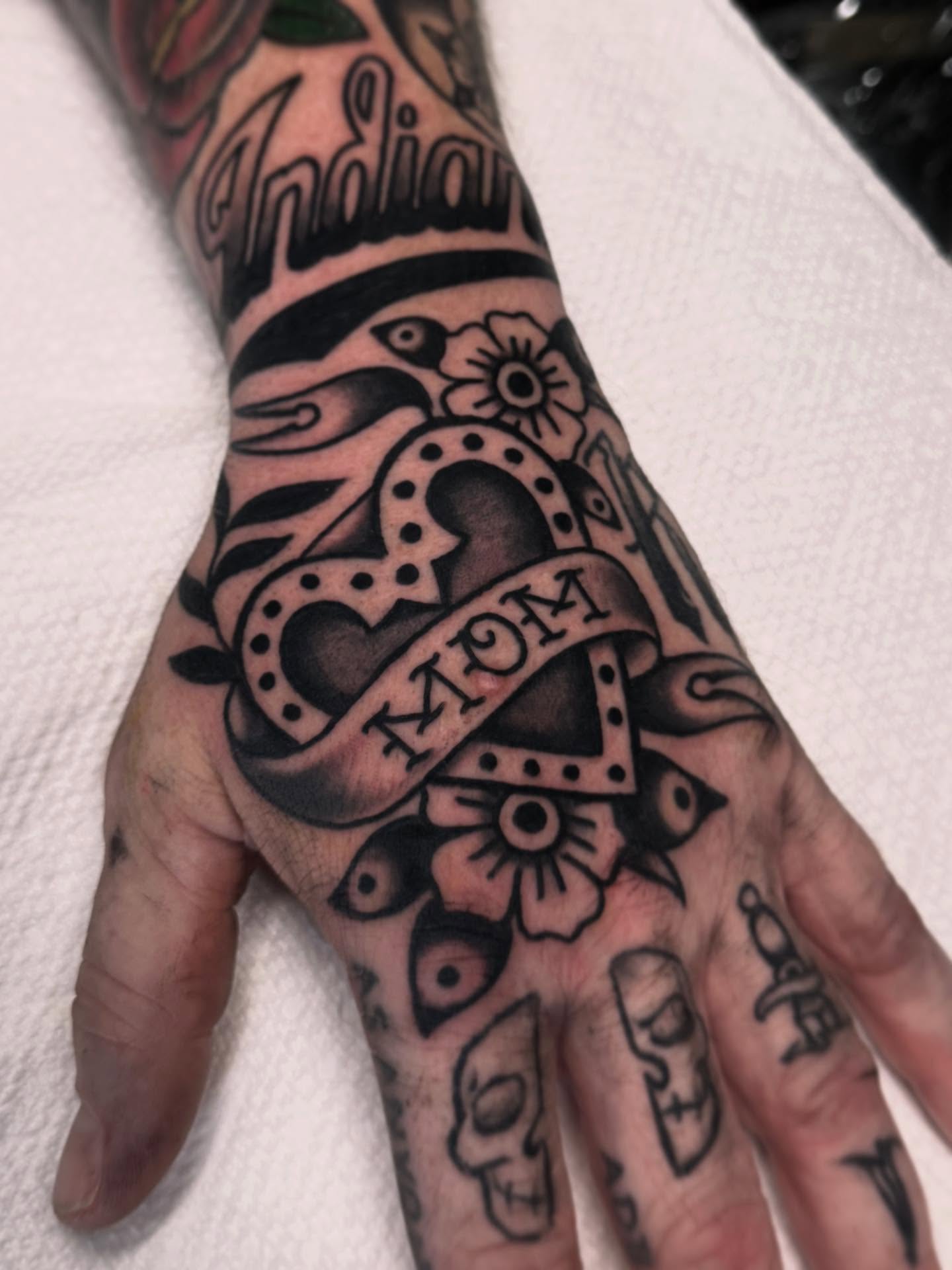 Infinity symbol with 'Mom' American traditional tattoo on the hand by Ryan Engels