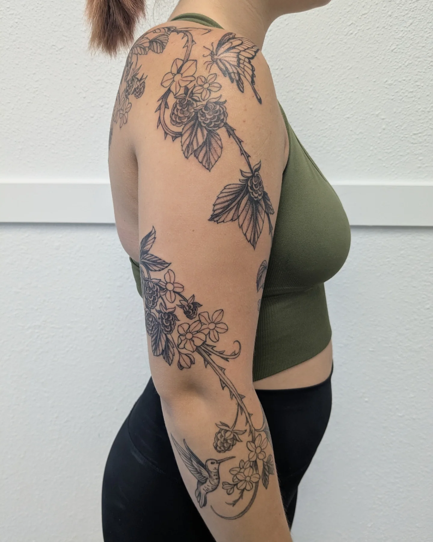 Floral vine with hummingbird black and grey tattoo on the upper arm by Ana Cielo Dueñas🌿Fernewt🌿Tattoo Artist🌿