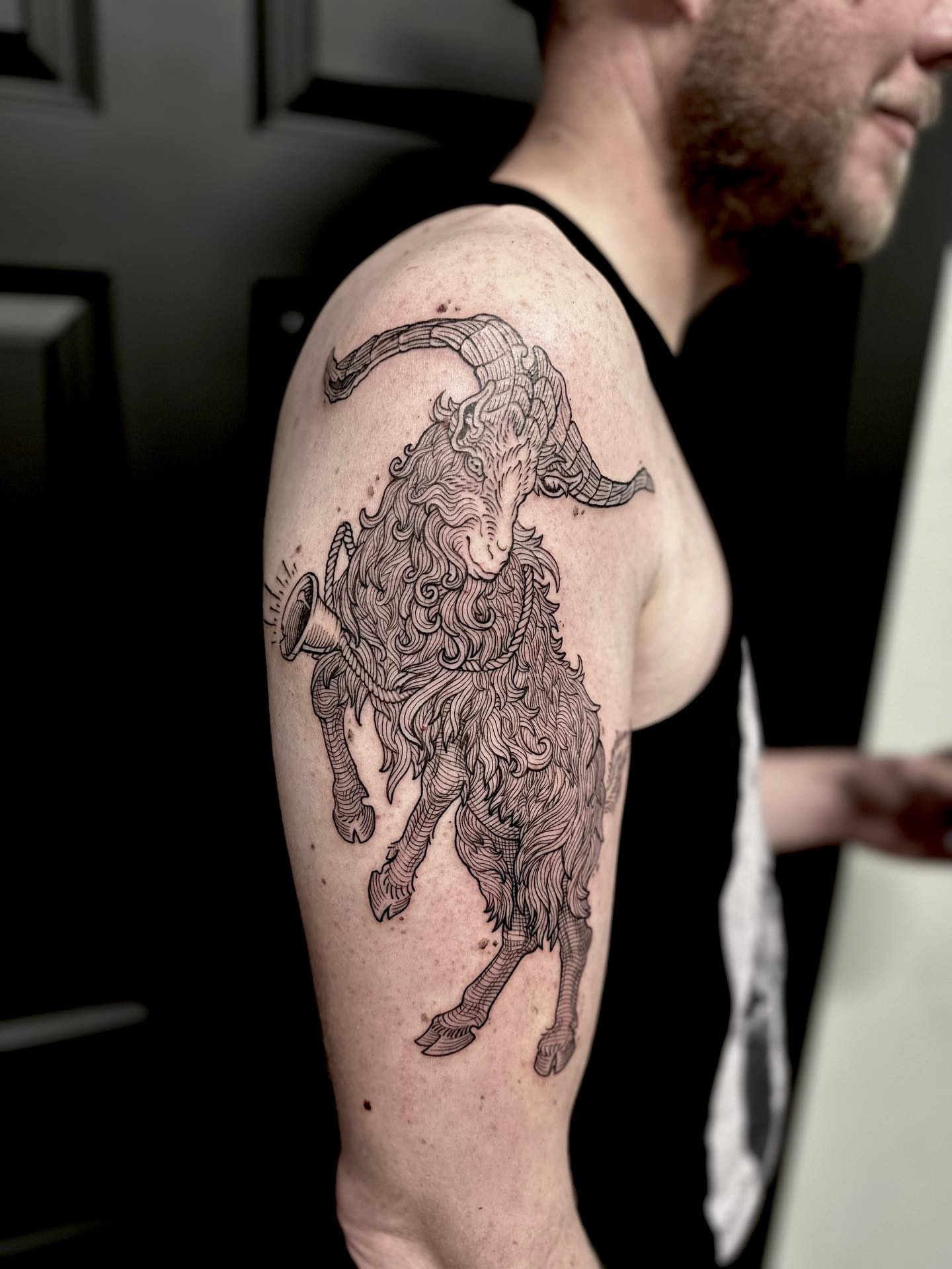 Goat with trumpet black and grey tattoo on the upper arm by Ciera High l Tattoo Artist