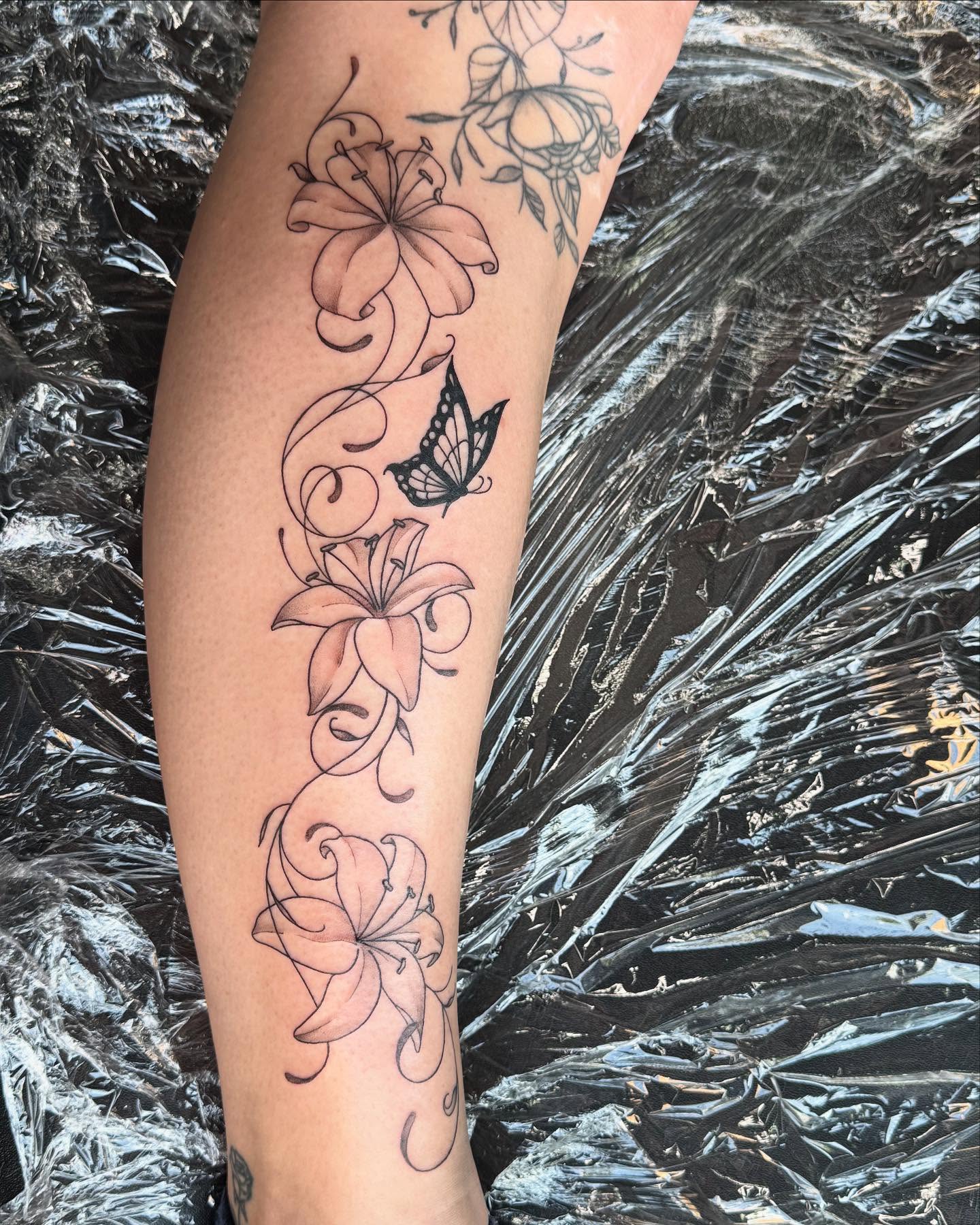 Flowers and butterfly watercolor tattoo on the forearm by Mickey