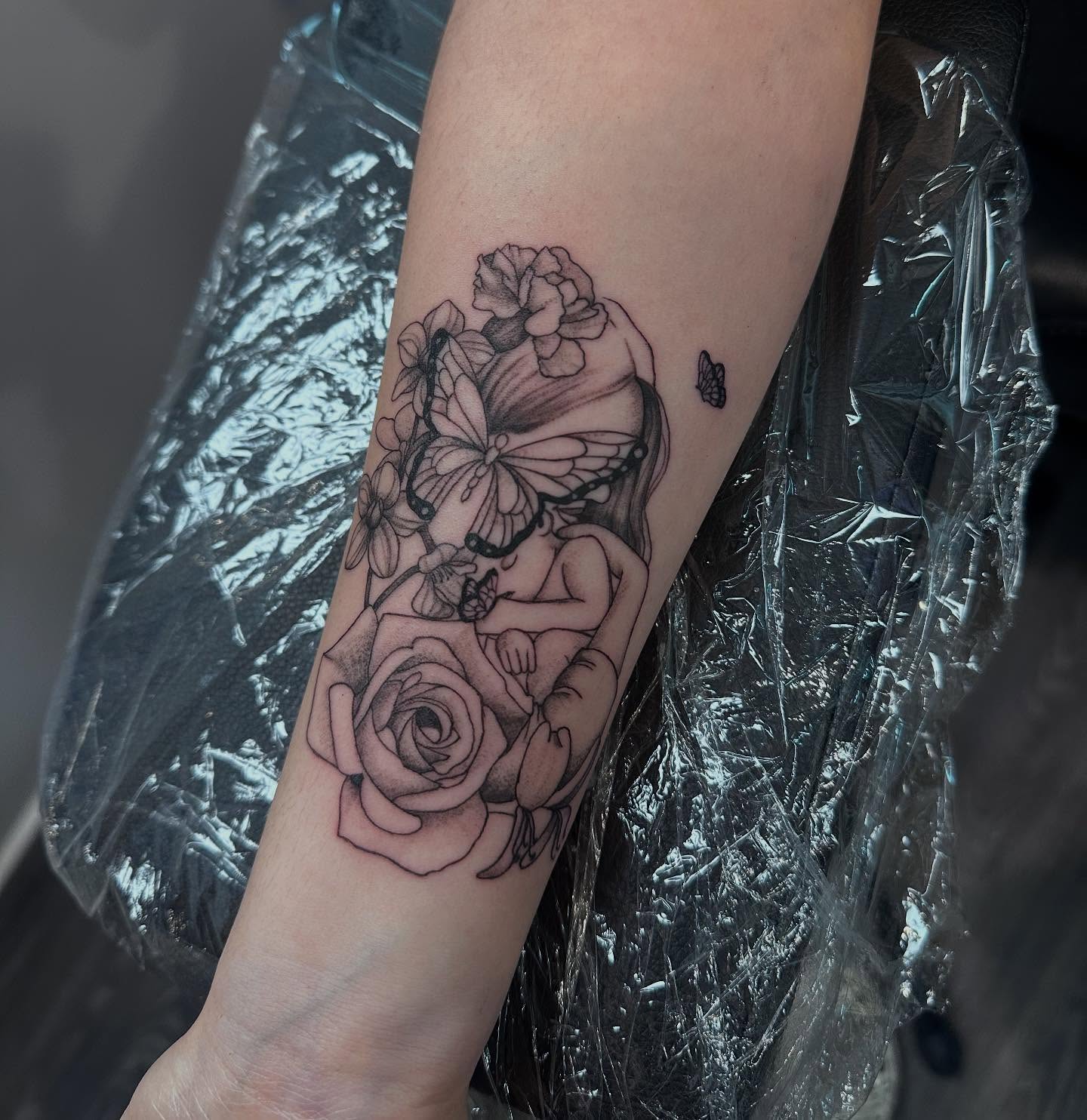 Baby with flowers black and grey tattoo on the forearm by Bell