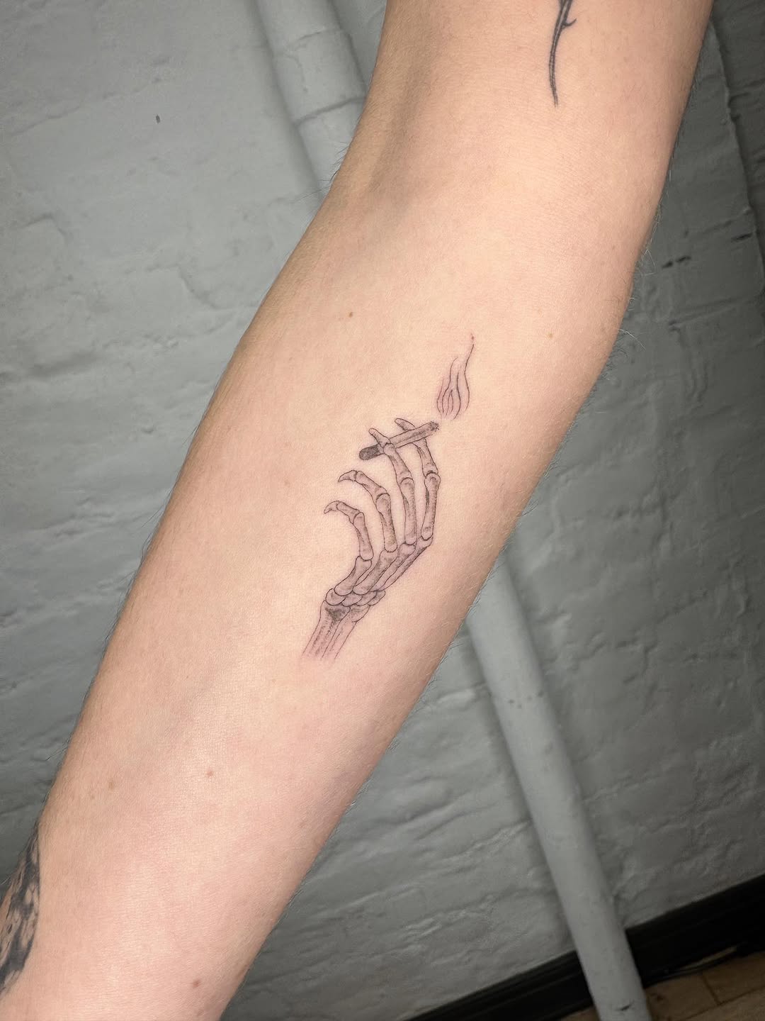 Skeleton hand holding cigarette sketch tattoo on the forearm by Jesus A.