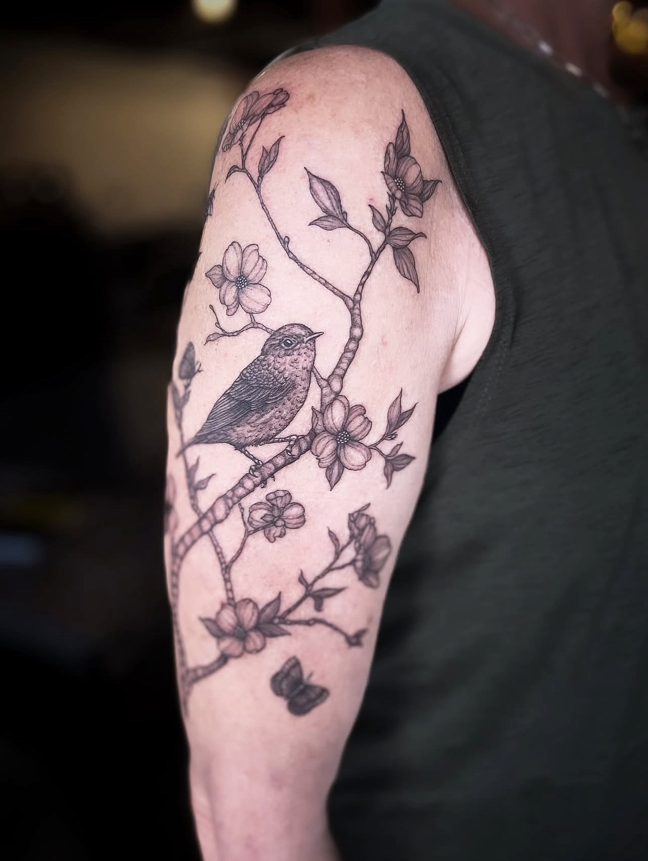 Bird and blossoms black and grey tattoo on the upper arm by 𝒥𝓊𝓃𝒾𝓅𝑒𝓇 𝒫𝑜𝓈𝓉 (Juju)