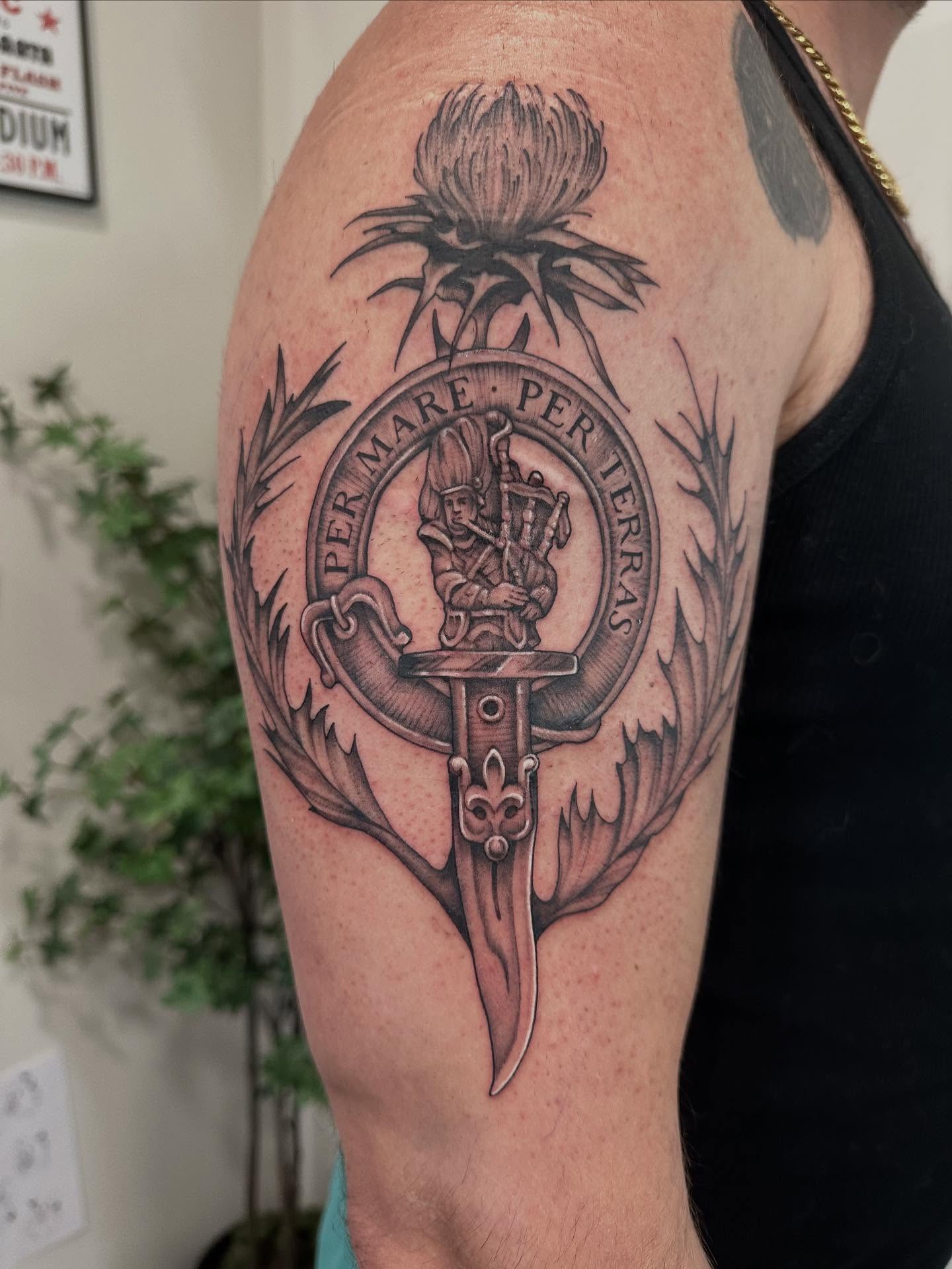 Clan crest black and grey tattoo on the upper arm by Kate Darling