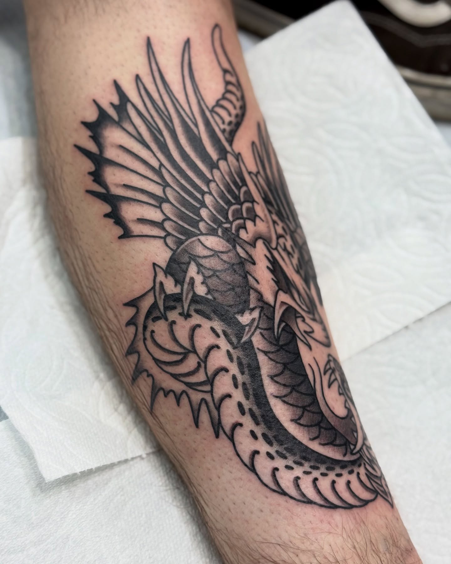 Winged dragon black and grey tattoo on the forearm by Ernie Rivera