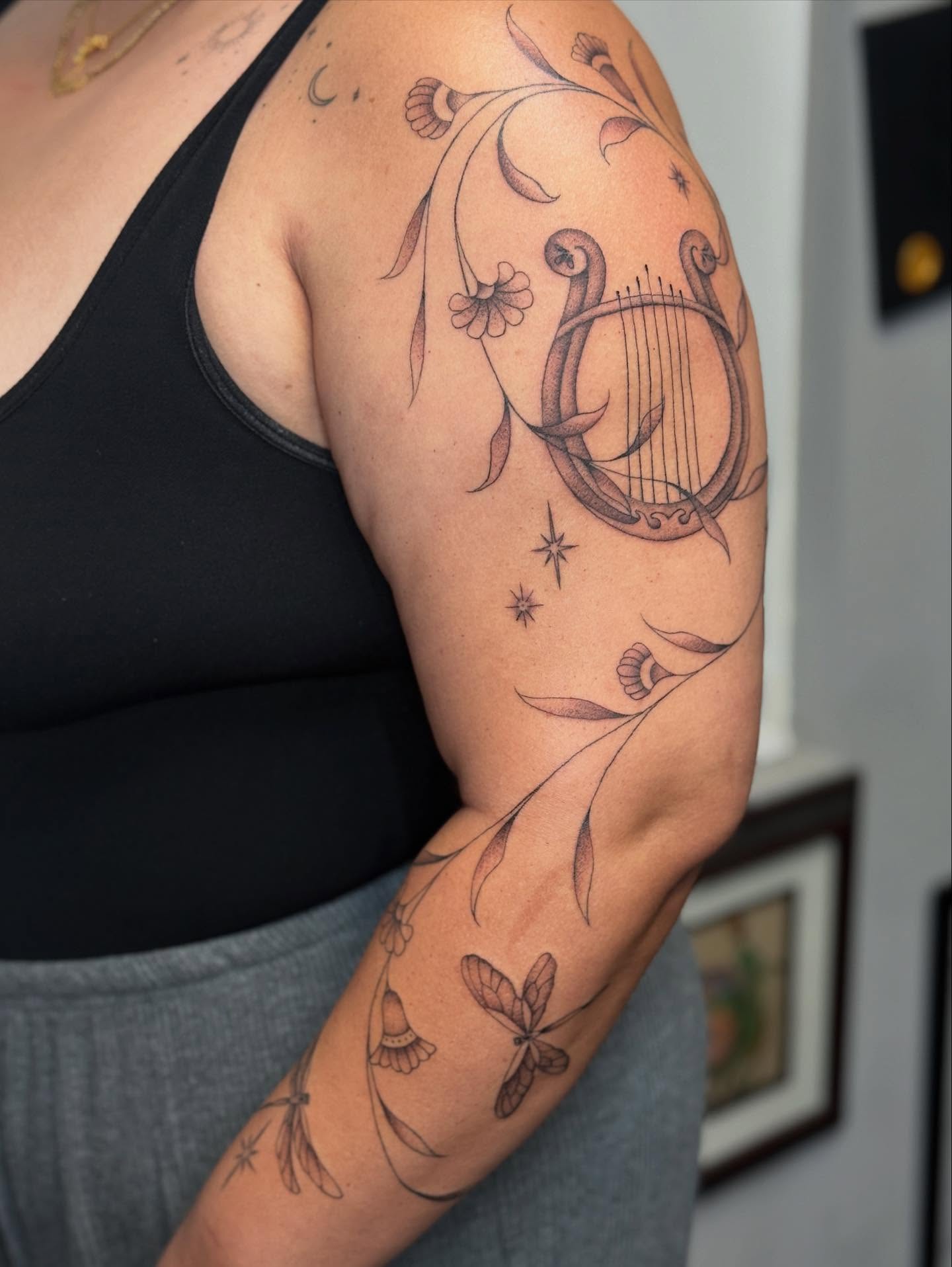 Lyre and floral black and grey tattoo on the upper arm by chloe jeanel estrada
