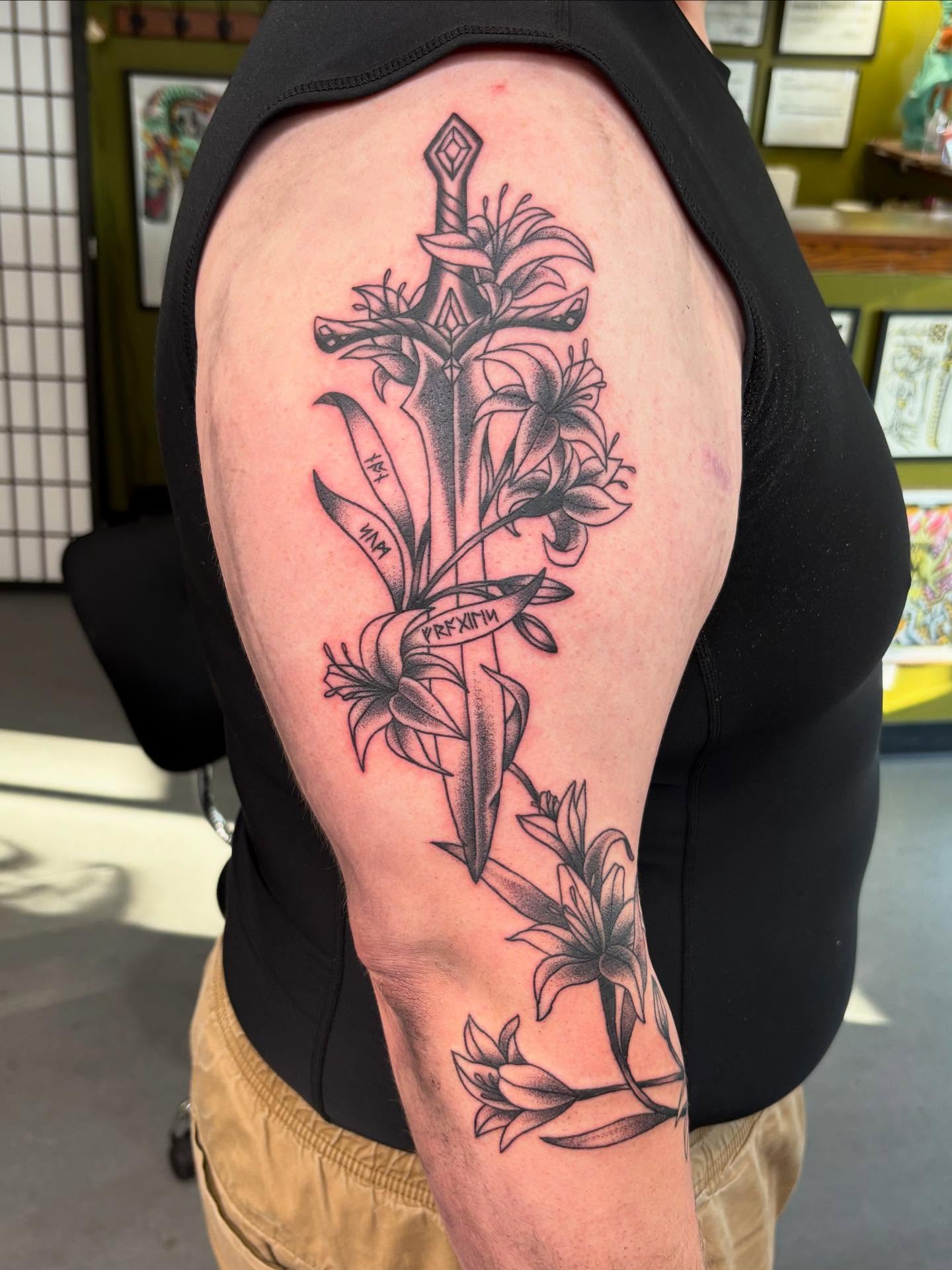 Sword and lilies black and grey tattoo on the shoulder by Jamie Yuu, Minneapolis, Minnesota