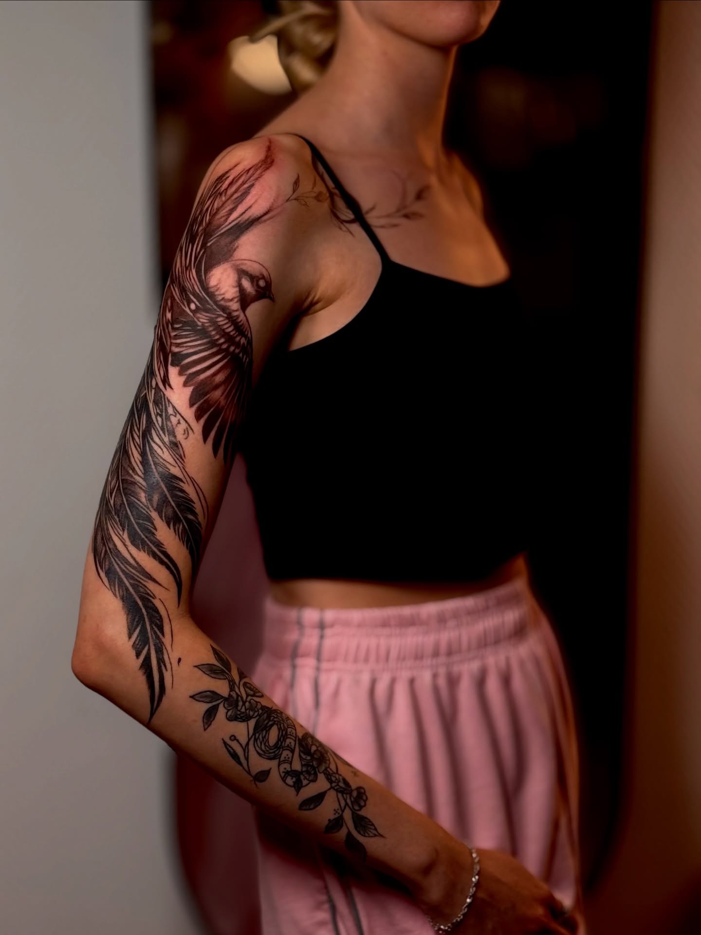 Feather and floral black and grey tattoo on the upper arm by Виктория Лукьянова