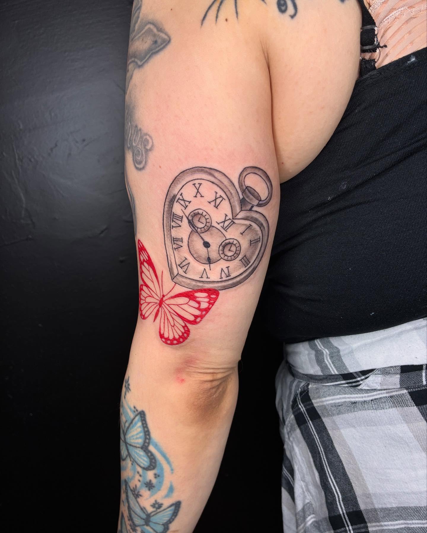 Heart-shaped pocket watch with butterfly realism tattoo on the forearm by Kat π
