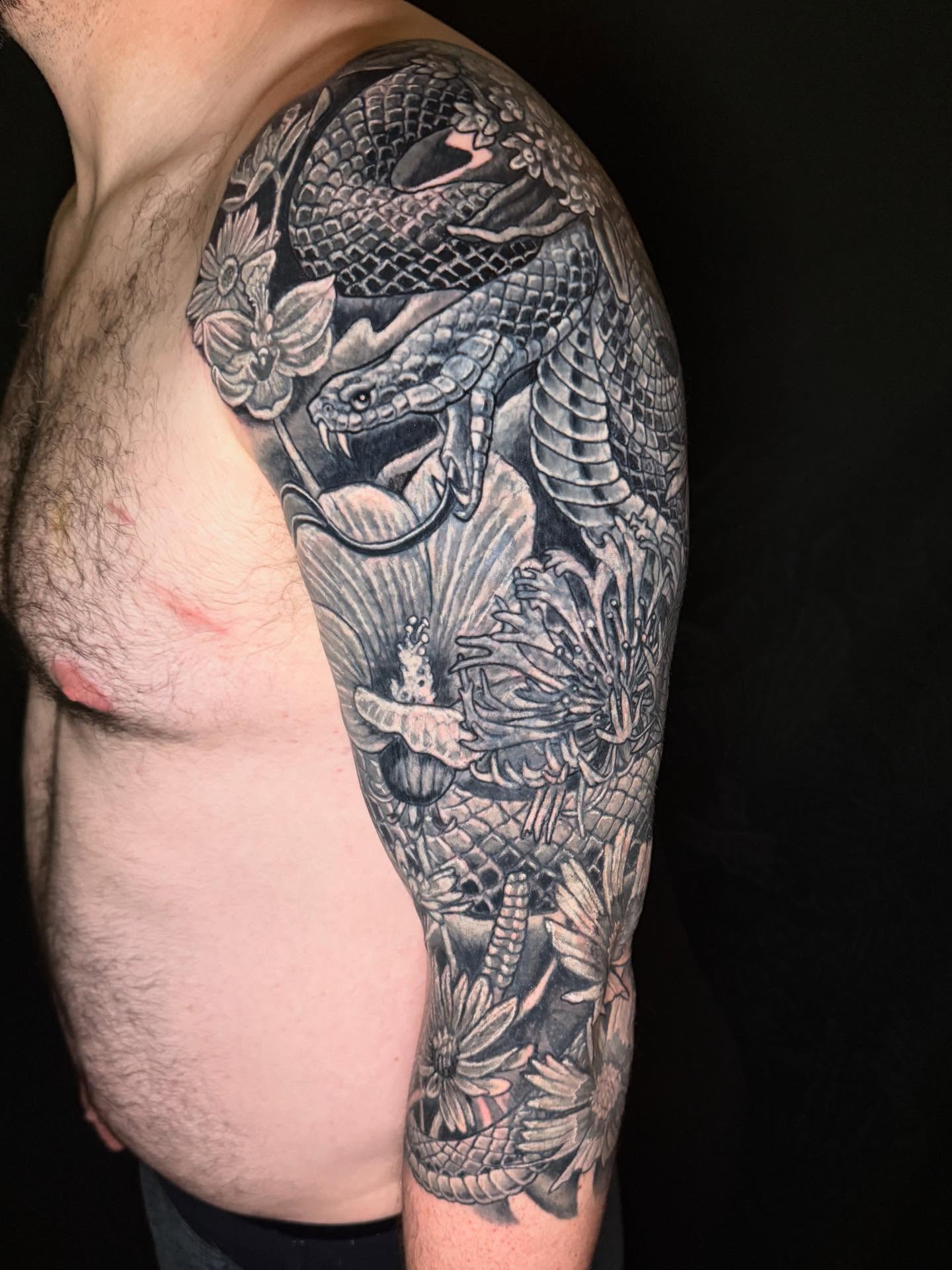 Snake and flowers realism tattoo on the upper arm by Patrick Cornolo