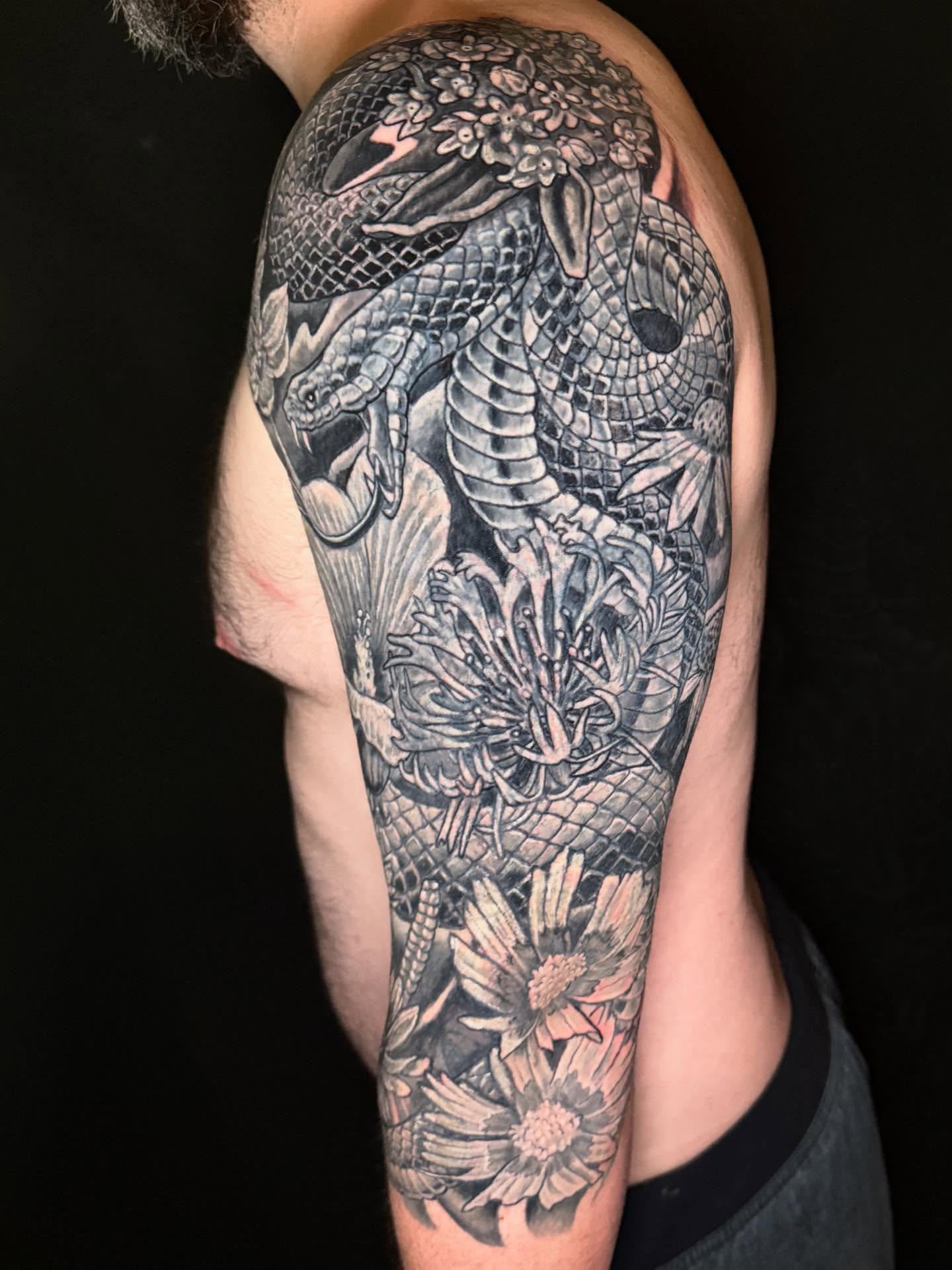 Snake and flowers realism tattoo on the upper arm by Patrick Cornolo