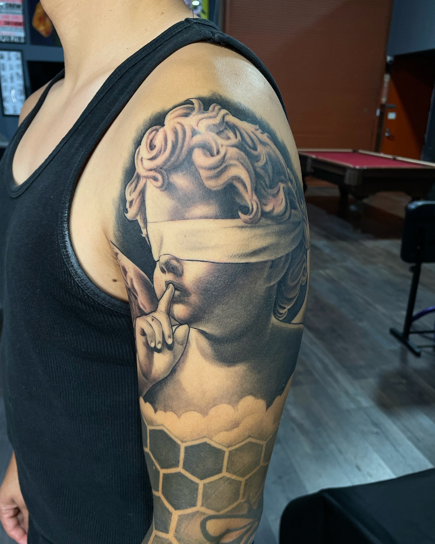 Statue realism tattoo on the upper arm by Alex Ortiz