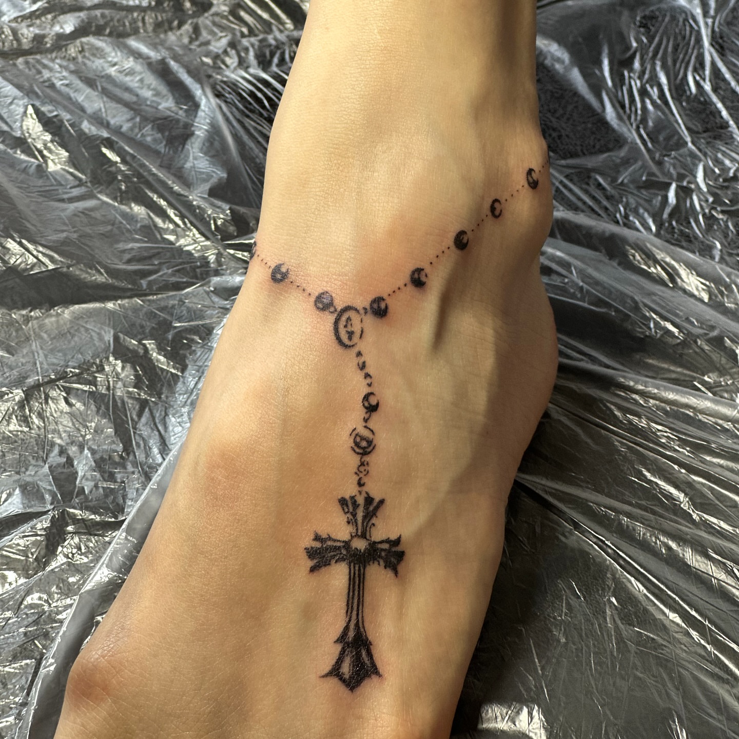 Cross and rosary dotwork tattoo on the foot by Casper Tattoos Toronto