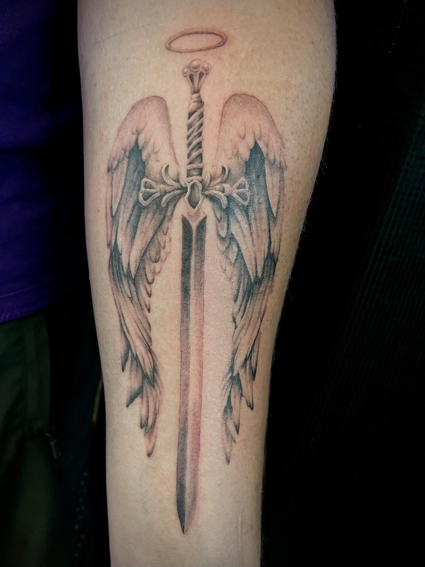 Sword with wings black and grey tattoo on the forearm by Bryce Presley, Mission, Kansas