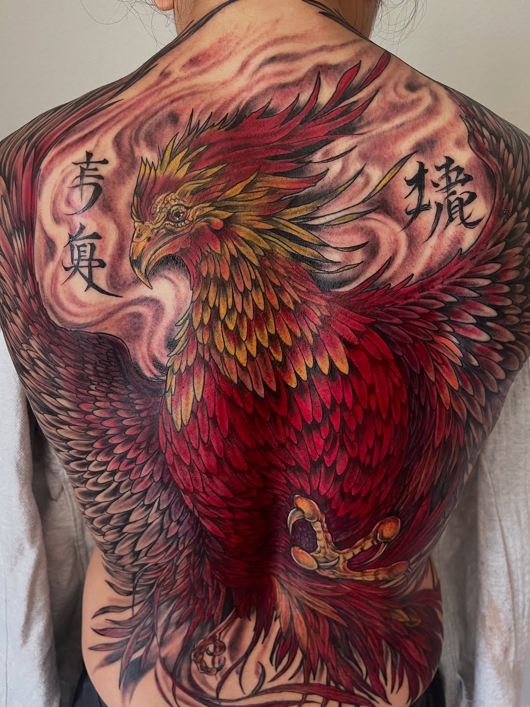 Phoenix with chinese characters realism tattoo on the back by Janelle Cuba