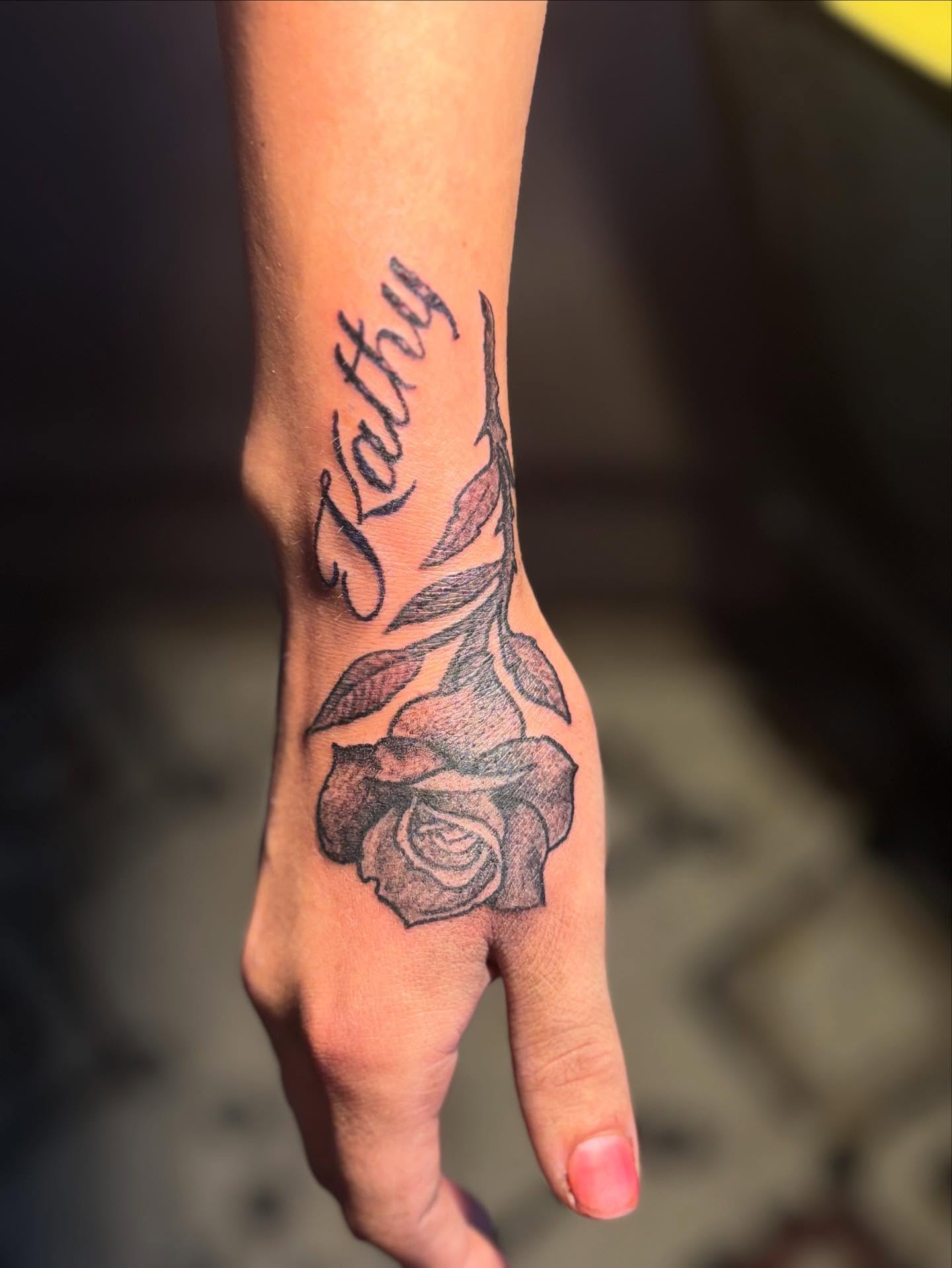 Rose and name black and grey tattoo on the hand by sams tattoos