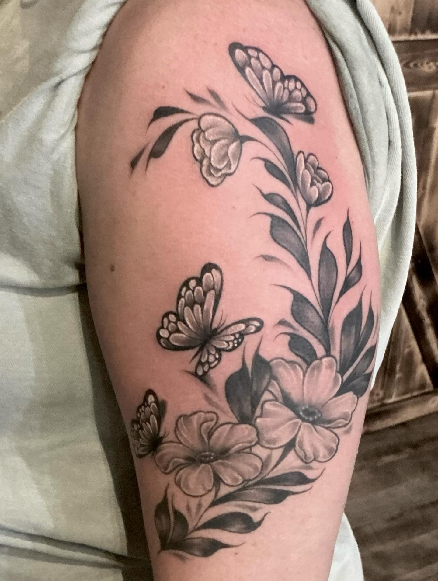 Flowers and butterflies black and grey tattoo on the upper arm by Heather Syvilla Tattoos