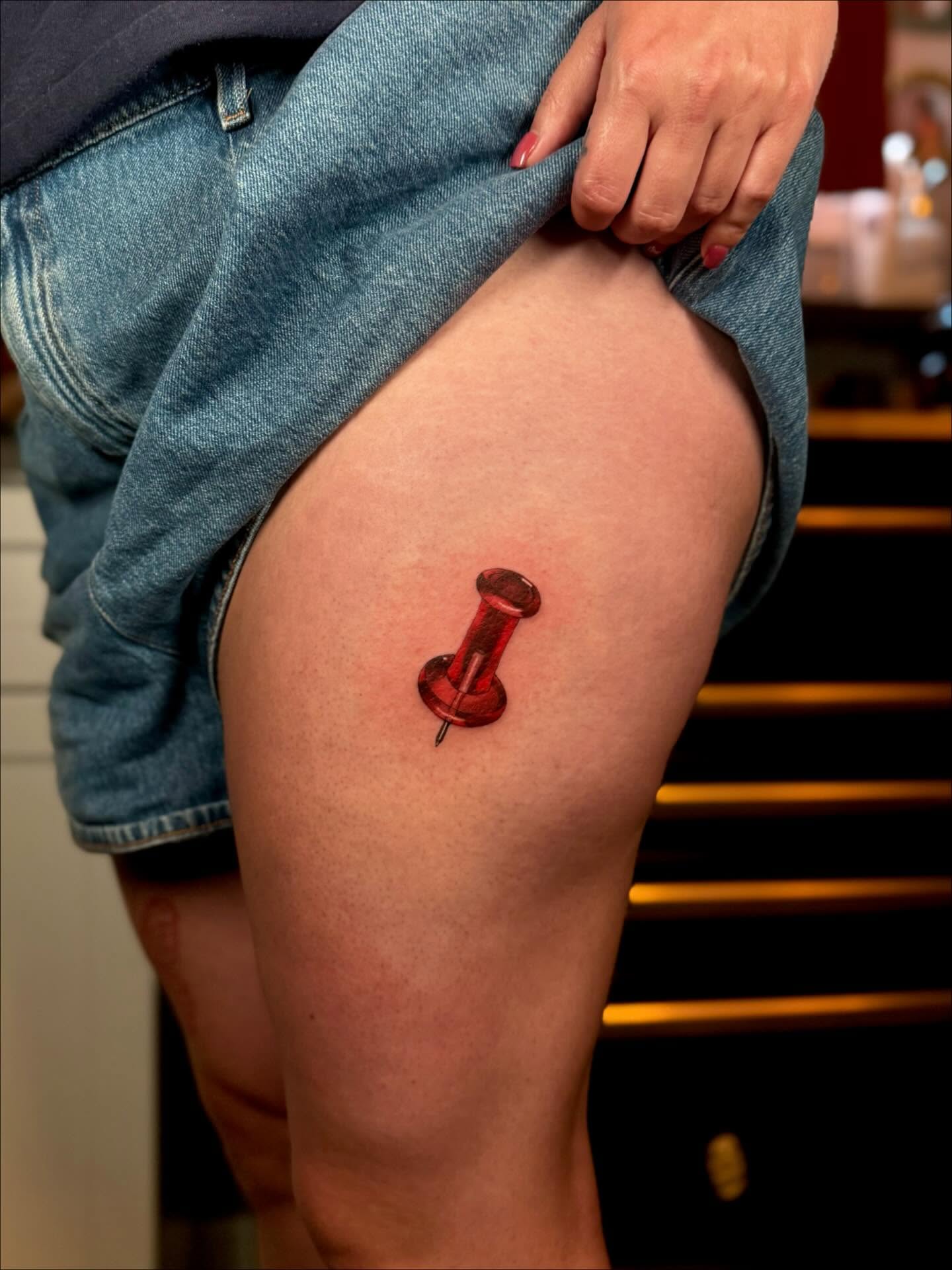 Red pushpin realism tattoo on the thigh by laura baldwin