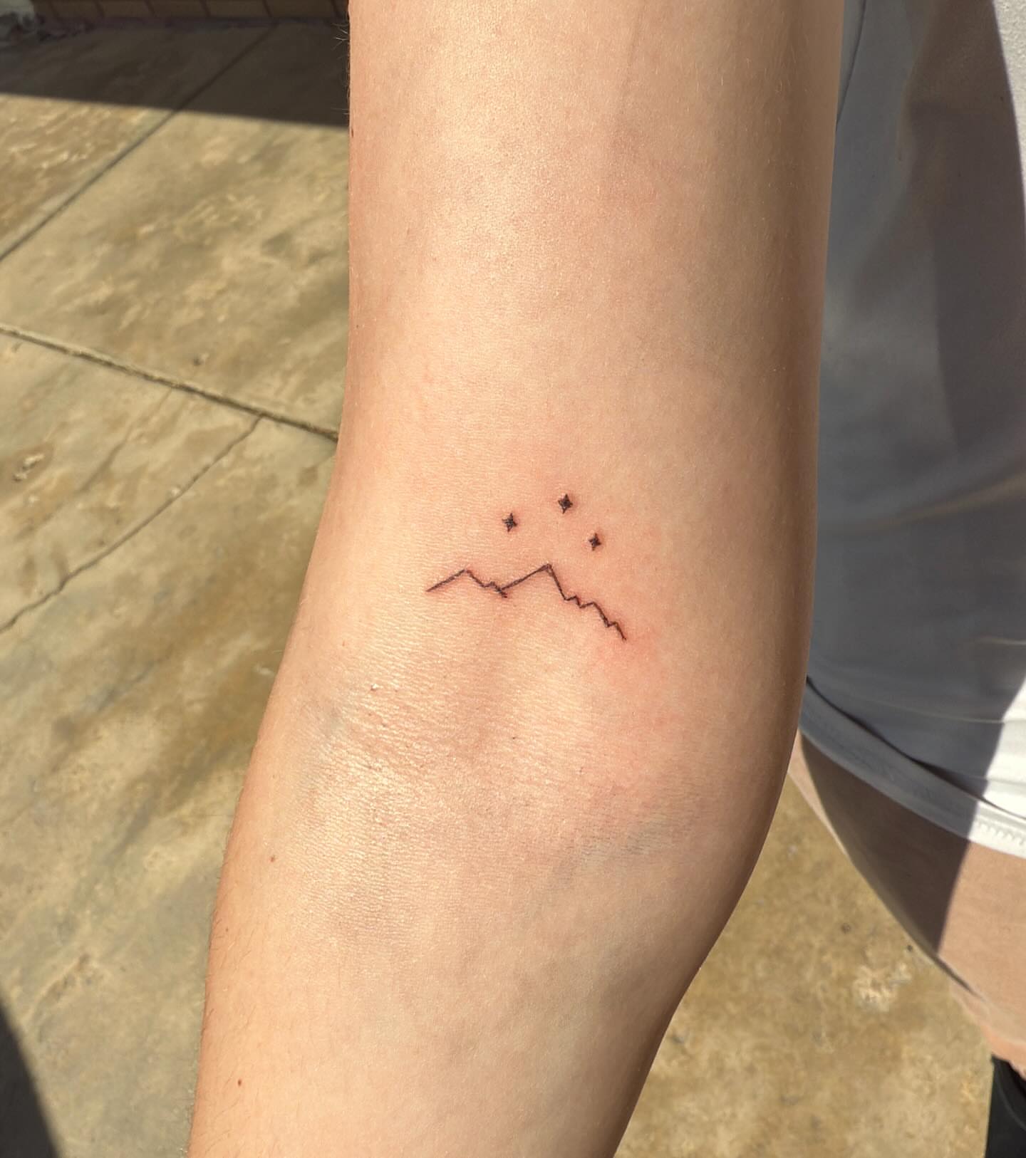 Mountain range with stars minimalist tattoo on the forearm by Kylee Snow