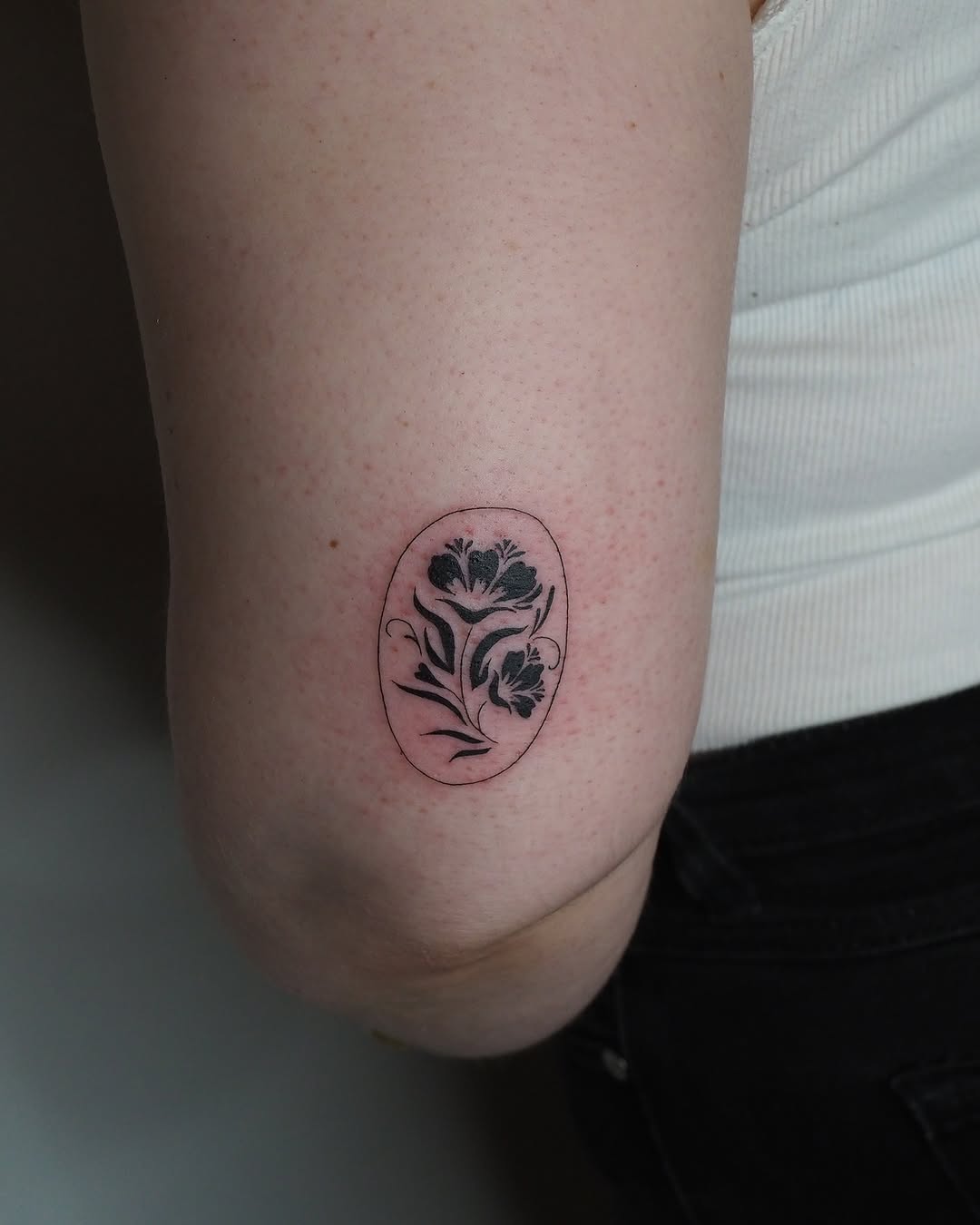 Flowers in an oval frame minimalist tattoo on the forearm by A. Eye Tat