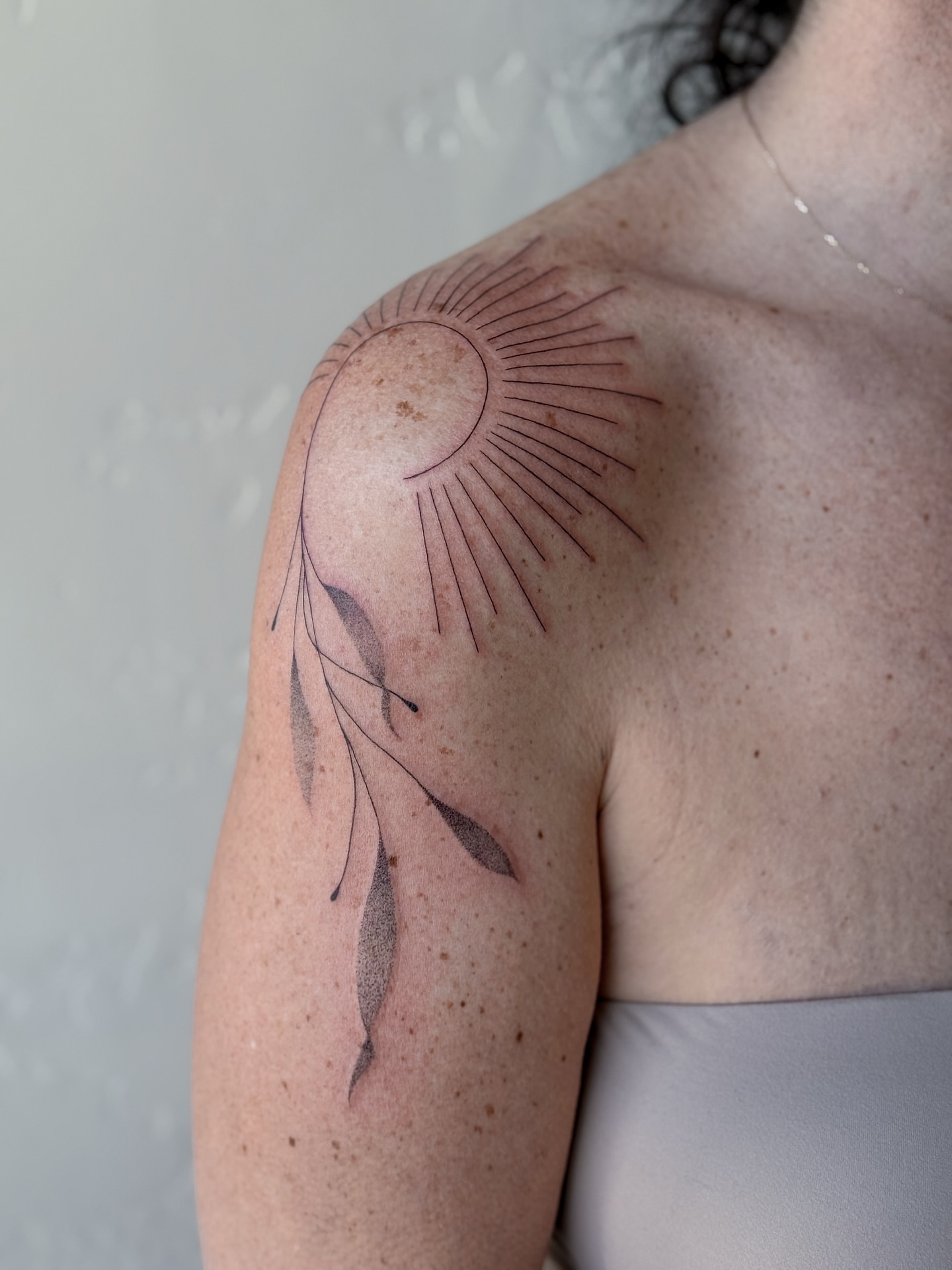 Sunburst and leaf fine line tattoo on the shoulder by Abby Robinson