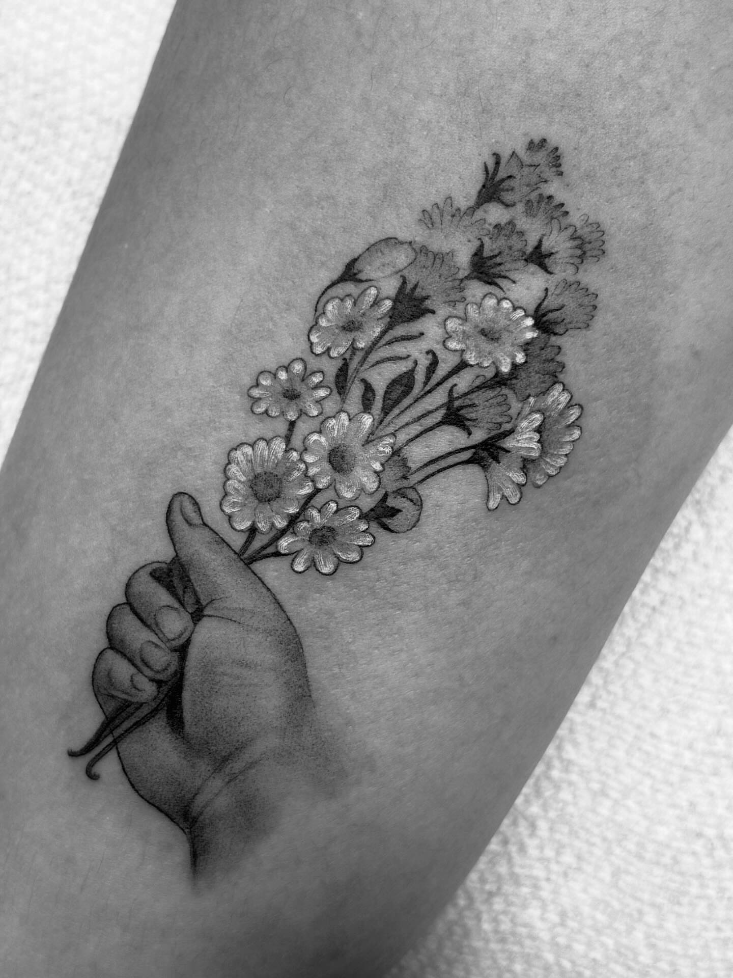 Hand holding flowers black and grey tattoo on the forearm by Storm