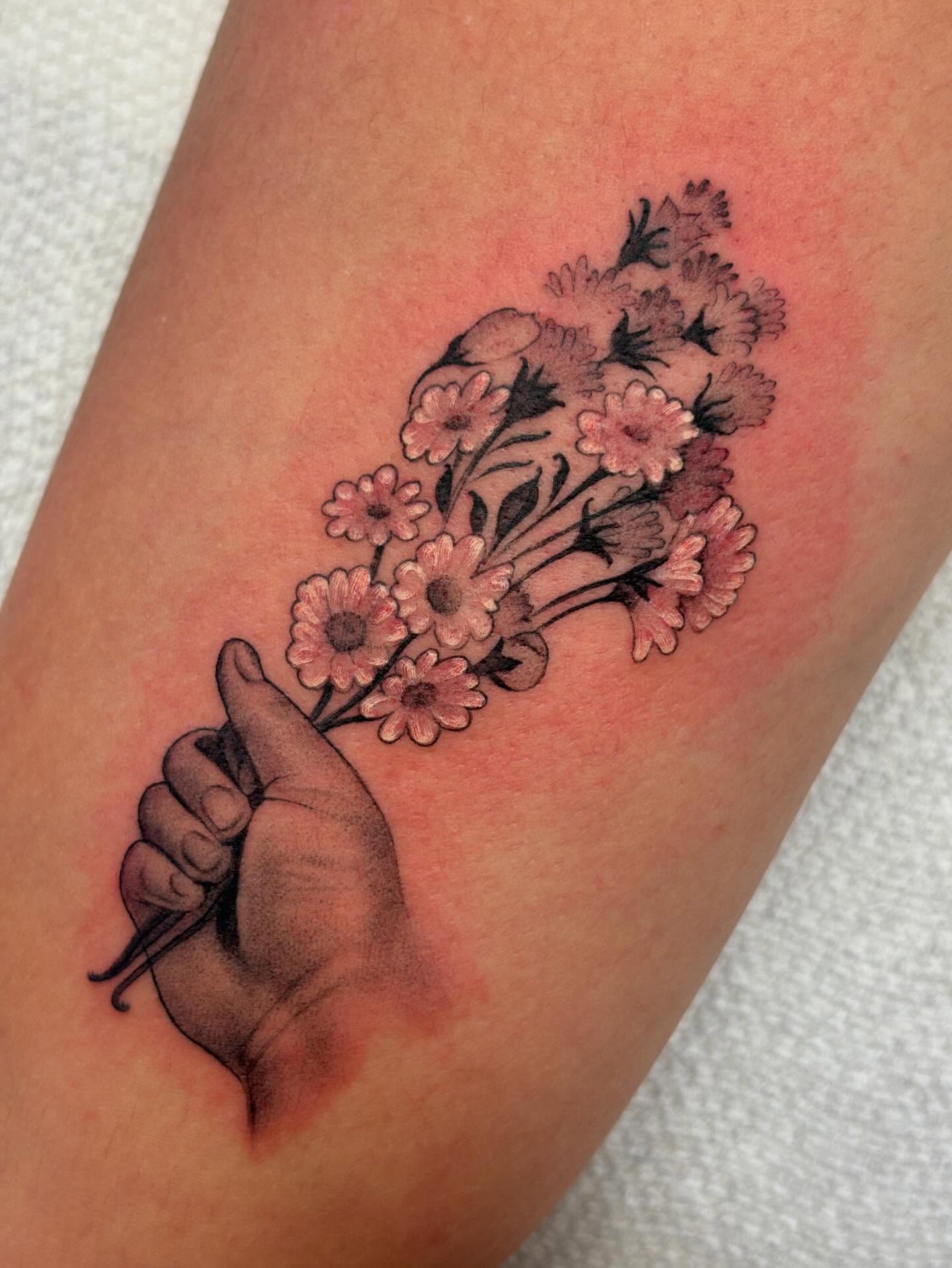 Hand holding flowers realism tattoo on the forearm by Storm