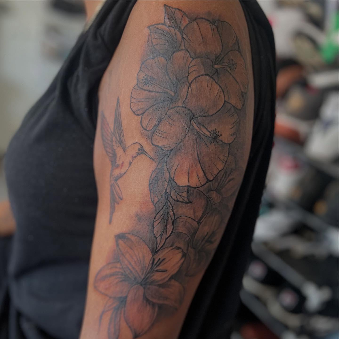 Flowers and hummingbird black and grey tattoo on the upper arm by Bris
