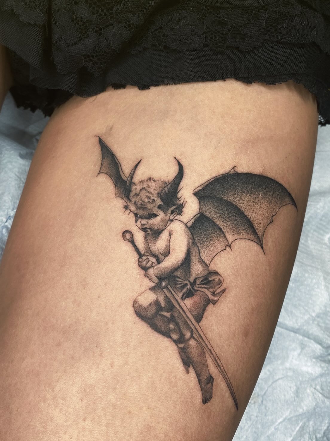 Cherub with bat wings black and grey tattoo on the thigh by Cody Mason
