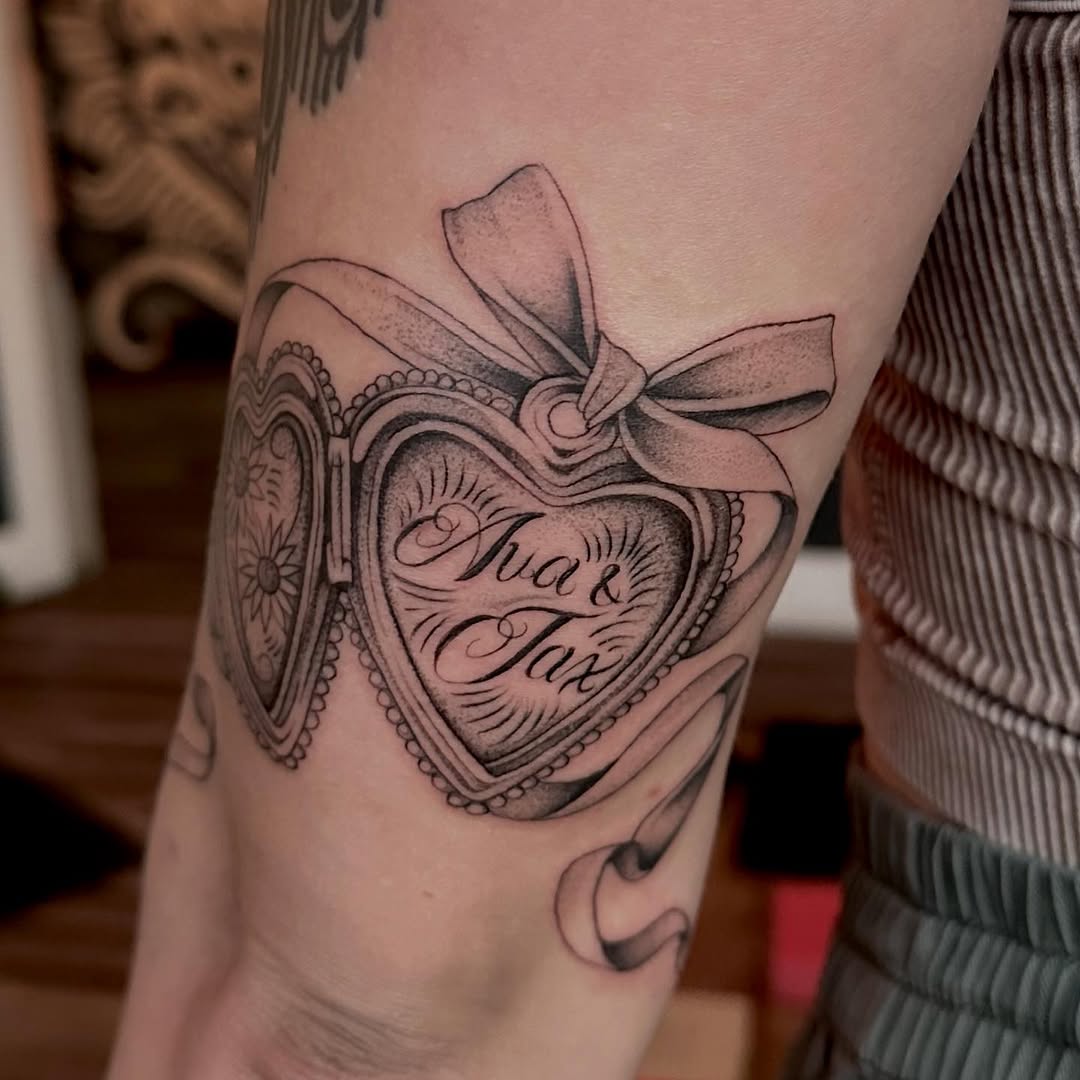 Heart locket with names tattoo on the forearm by Lia Massari