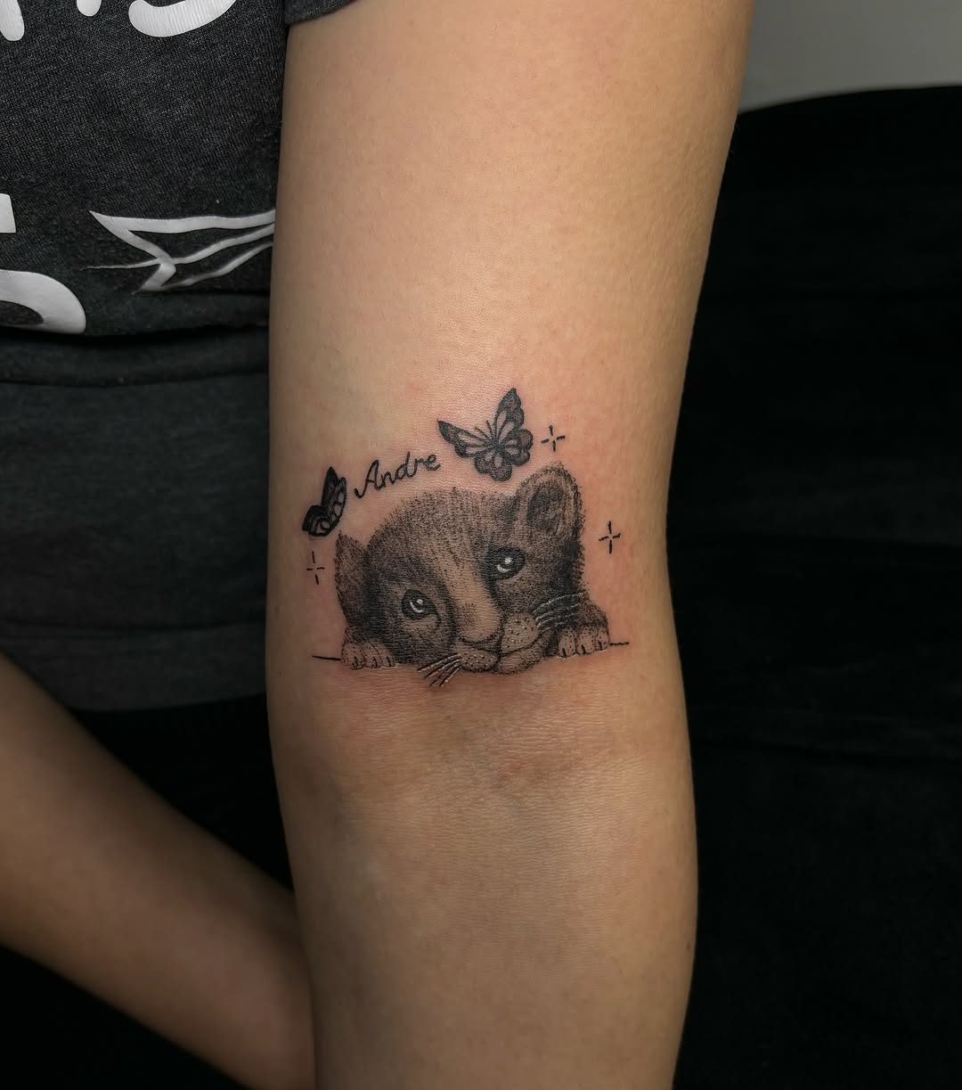 Lion cub with butterflies and name tattoo on the forearm by Victoria